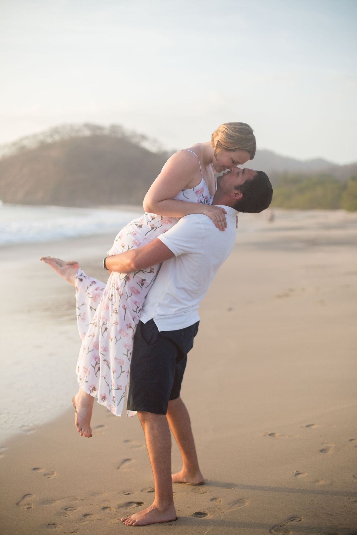 A woman being lifted into the air kissing her husband on a beach in costa rica