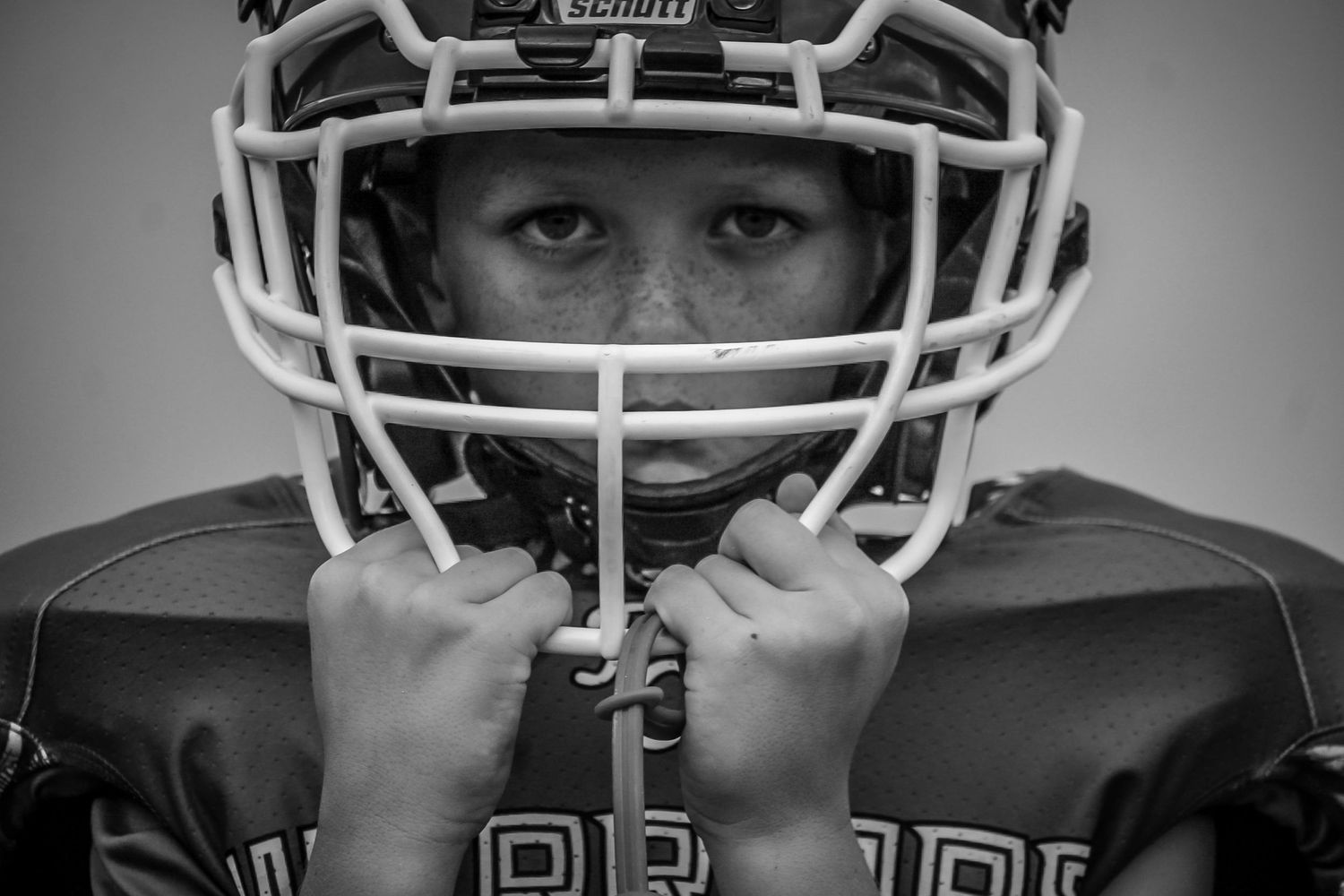 Young football player in Schutt helmet holding face mask in black and white portrait.