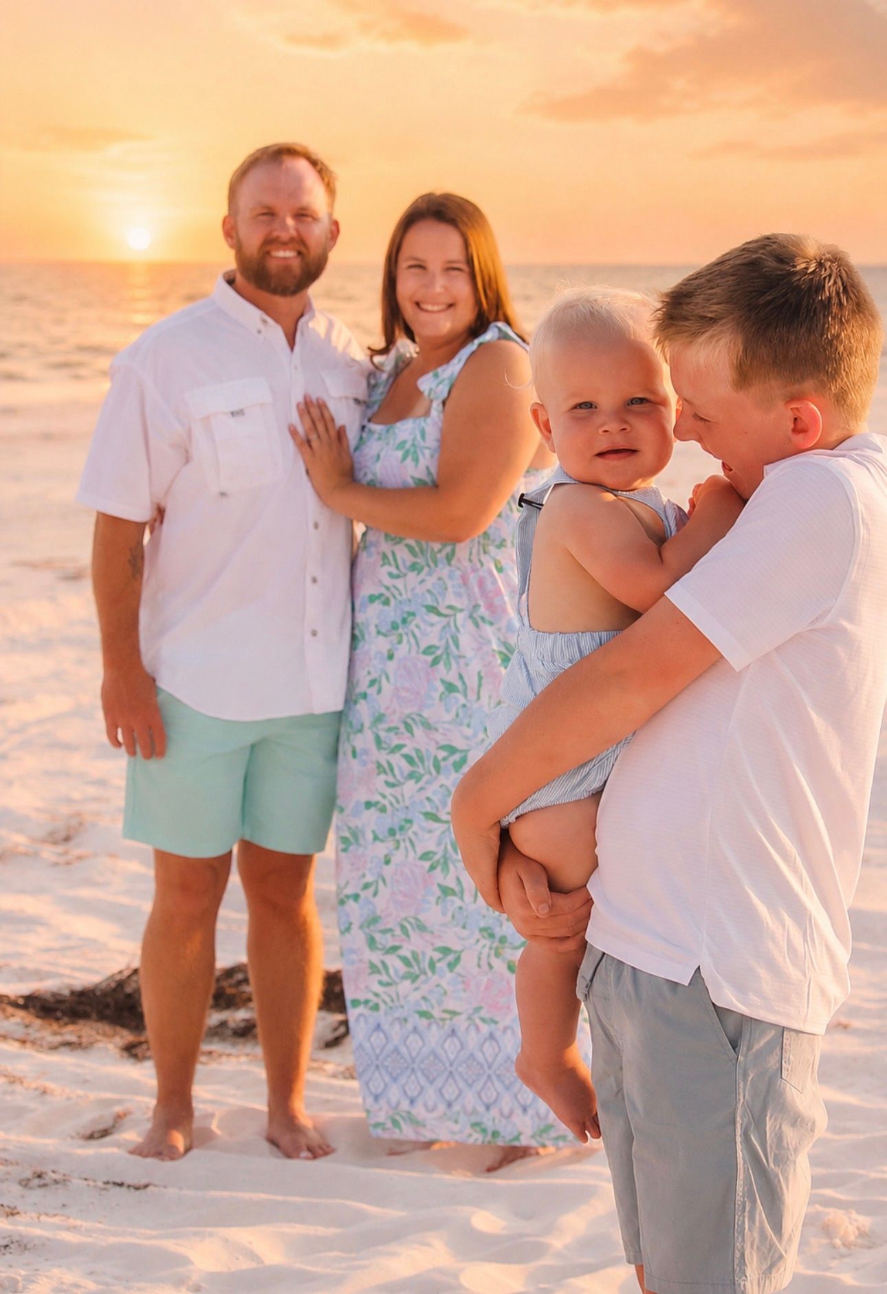 Family of four enjoying a golden sunset beach photo session, with parents and two children on white sand.