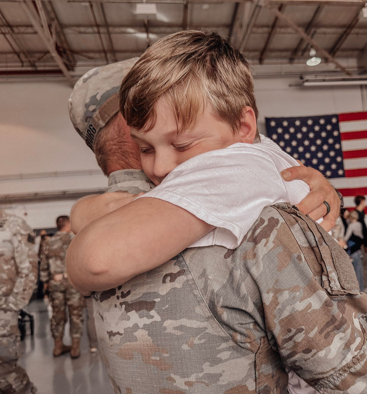 Emotional military homecoming as a soldier in camouflage hugs a young boy in a hangar.