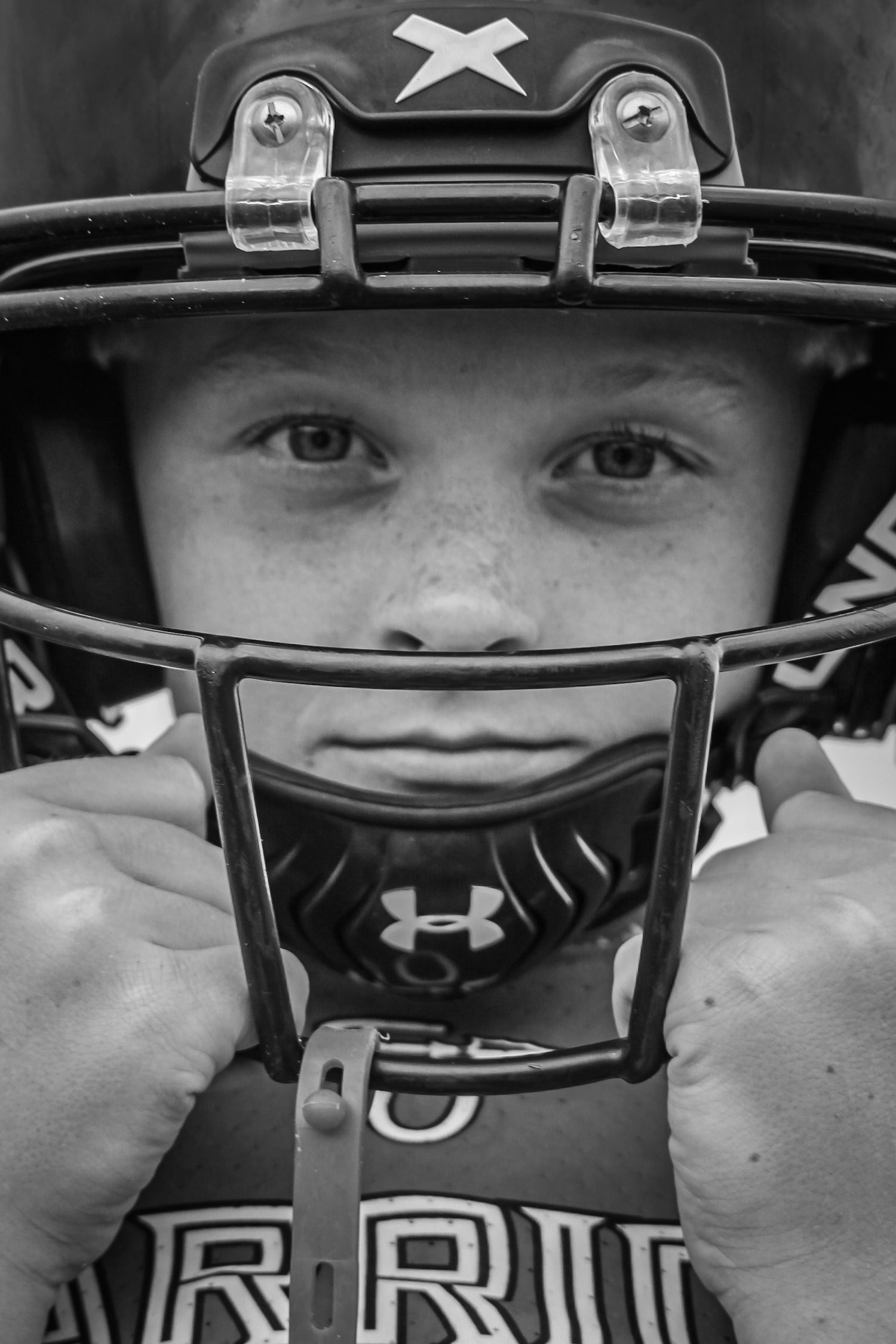 Black and white portrait of a young boy wearing a football helmet with face guard and Under Armour mouthguard.