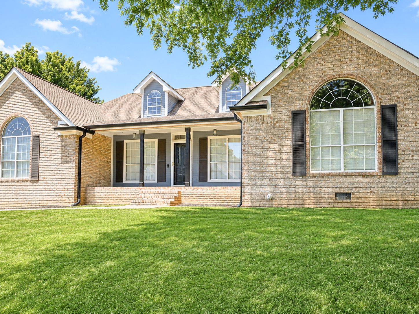 Traditional brick ranch home with covered porch, arched windows, and lush green lawn.