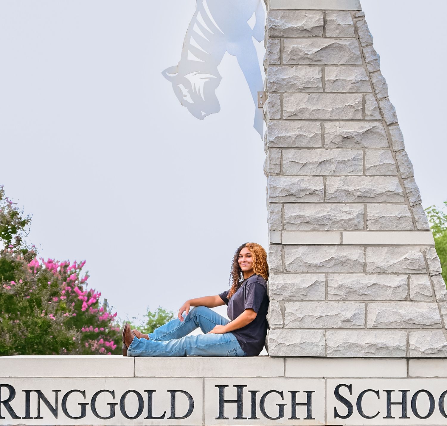 High school senior girl sits casually on Ringgold High School monument sign with horse mascot statue behind her.