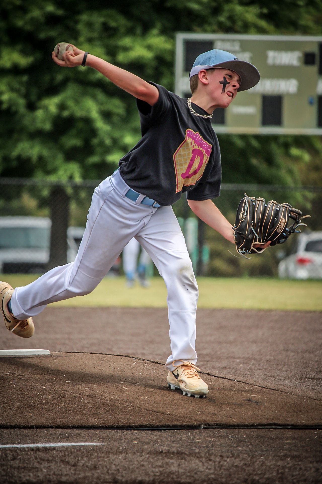 Young baseball pitcher in black jersey and white pants winds up to throw during a youth league game outdoors.