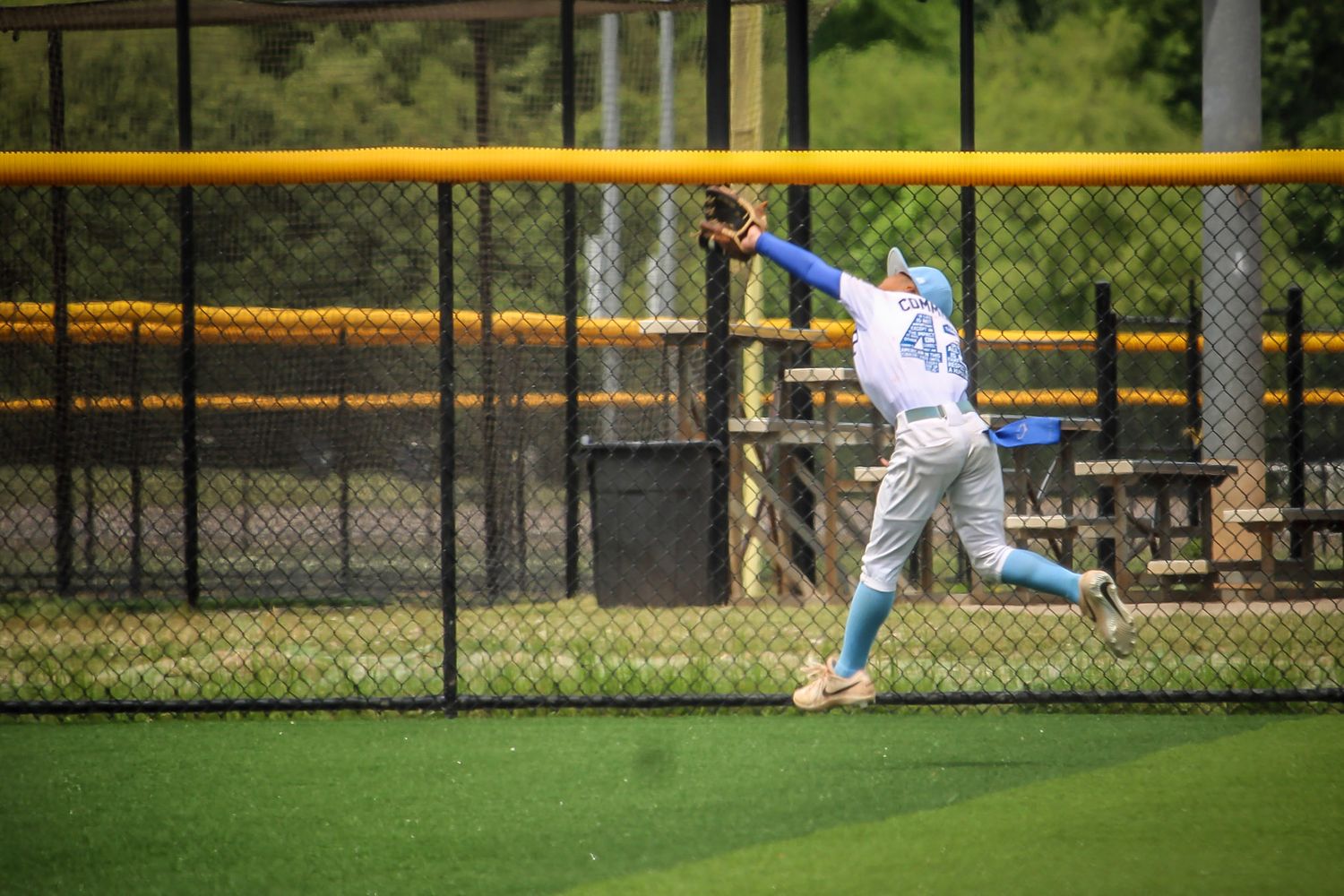 Baseball outfielder in light blue uniform reaching up to catch a fly ball.