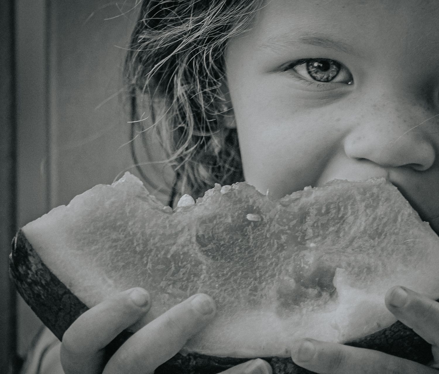 Black and white photo of a young child eating a large slice of watermelon, close-up shot.