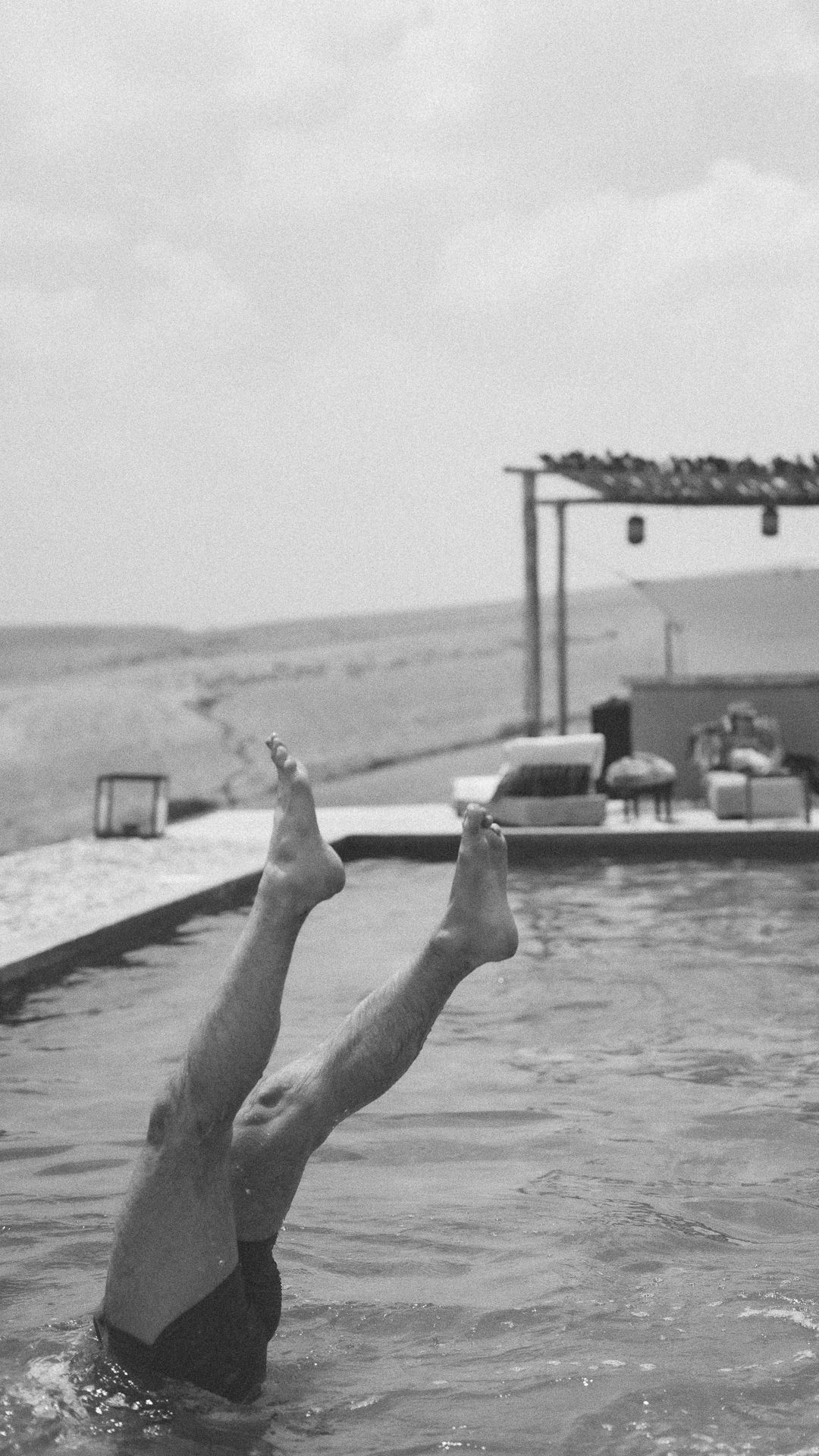 Black and white photo of person diving into infinity pool with desert landscape.
