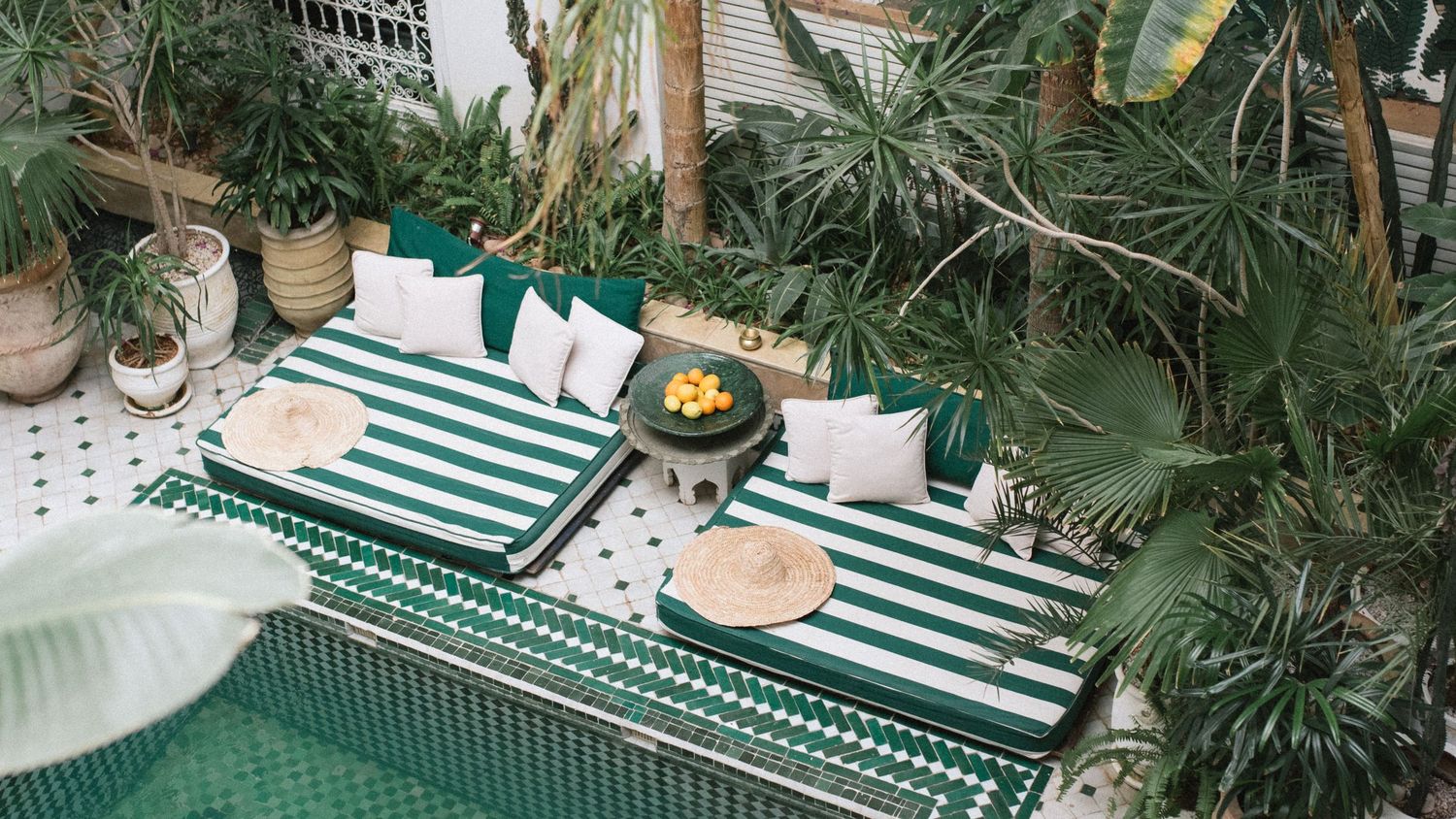 Aerial view of a green and white striped outdoor dining table set with cushions surrounded by tropical plants.