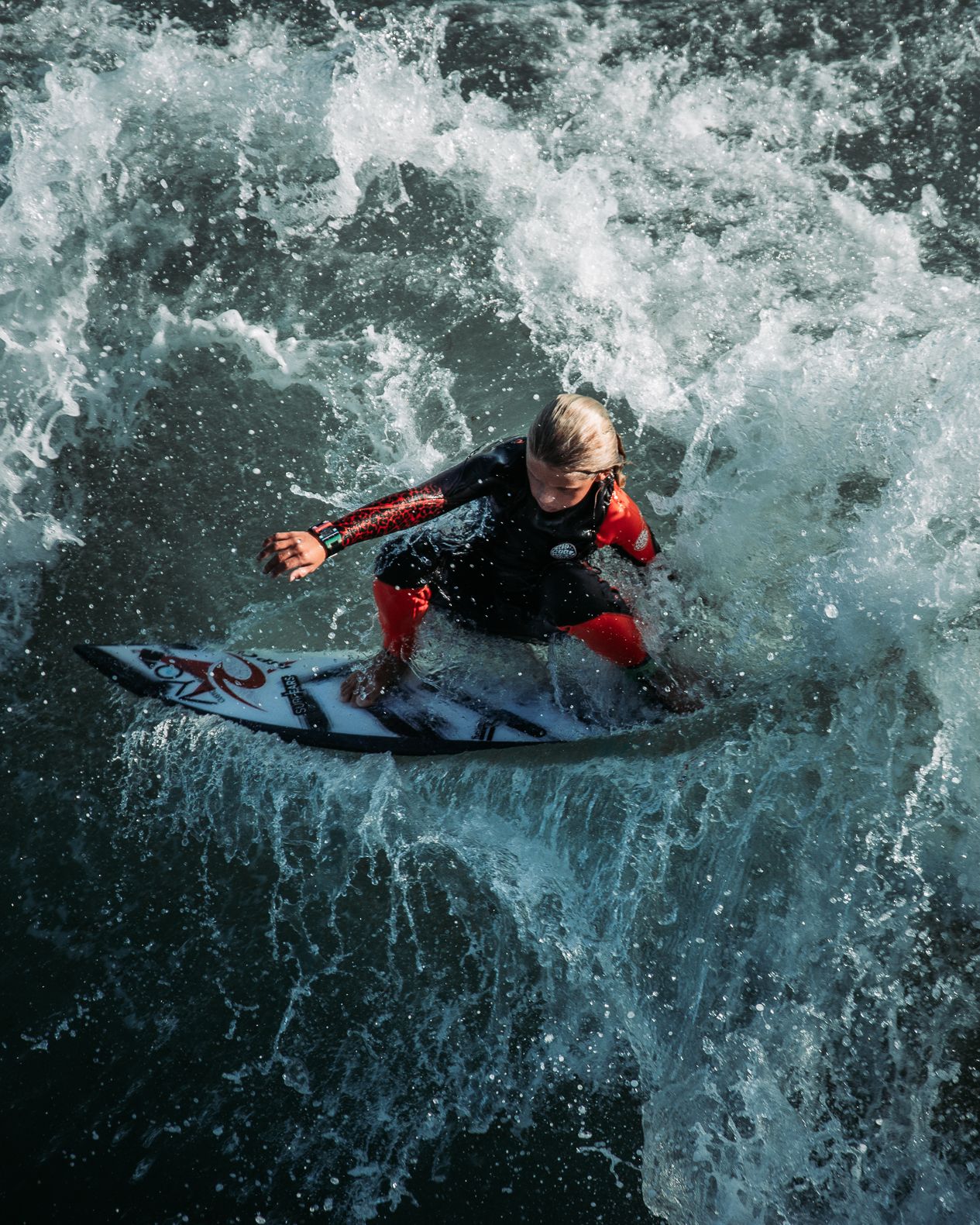 Aerial view of a young surfer riding a powerful wave in a black and red wetsuit.