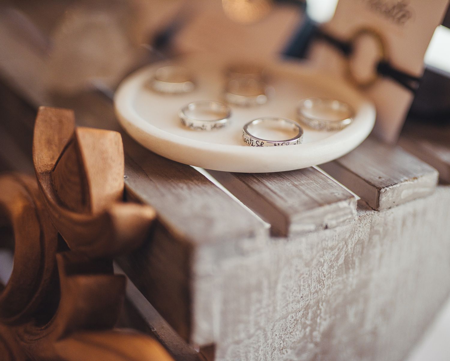 Silver rings displayed on a small white ceramic tray atop a rustic wooden box.