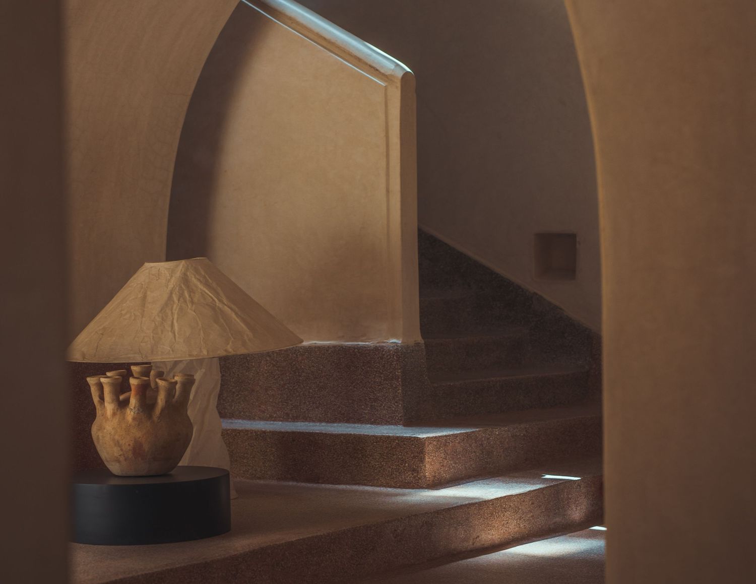 Warm-toned interior staircase with arched walls and a rustic lamp casting soft shadows.