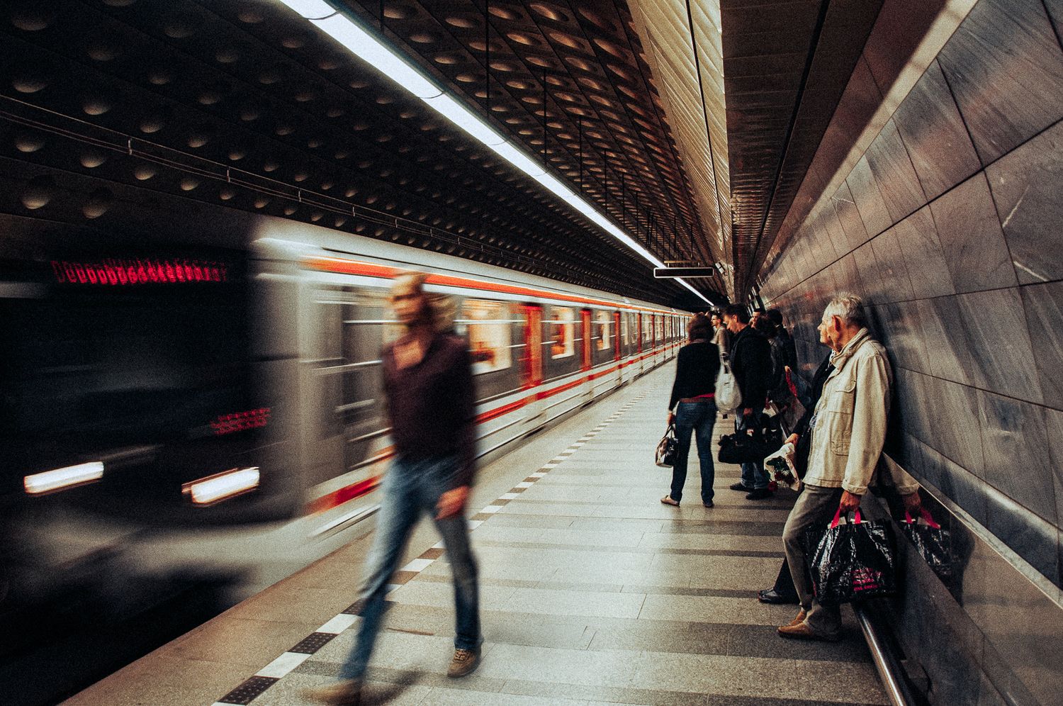 Blurred metro train arriving at underground station platform with passengers waiting along curved tunnel wall.
