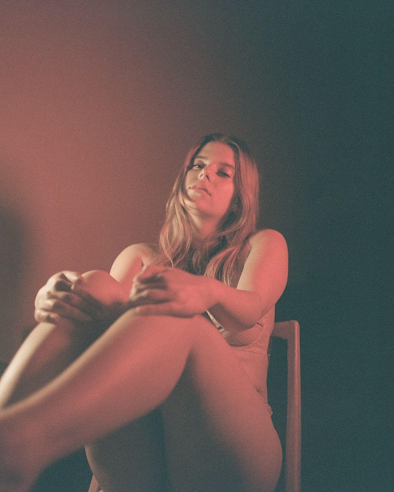 Moody portrait in warm tones of person sitting on chair in dramatic lighting.