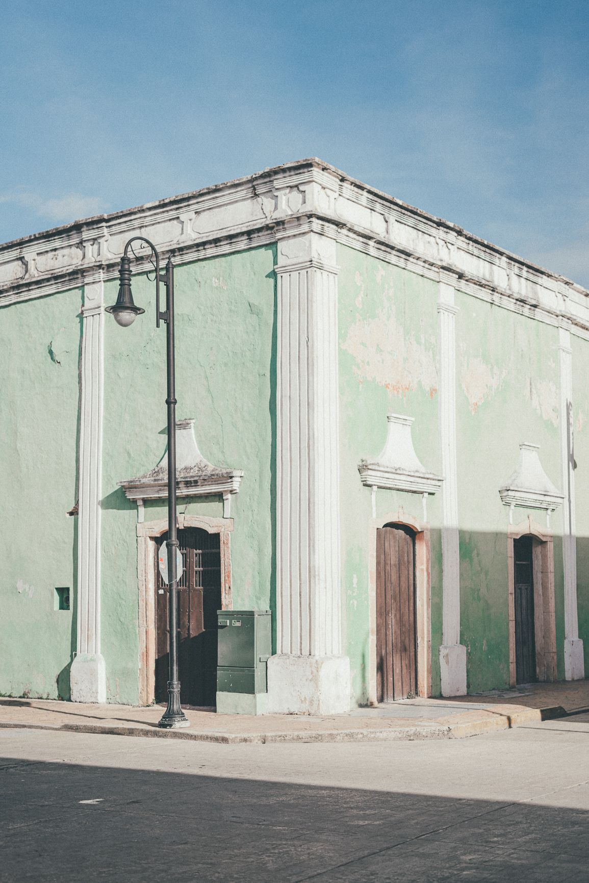 Corner of a vintage mint green colonial building with white pilasters and a street lamp under blue sky.
