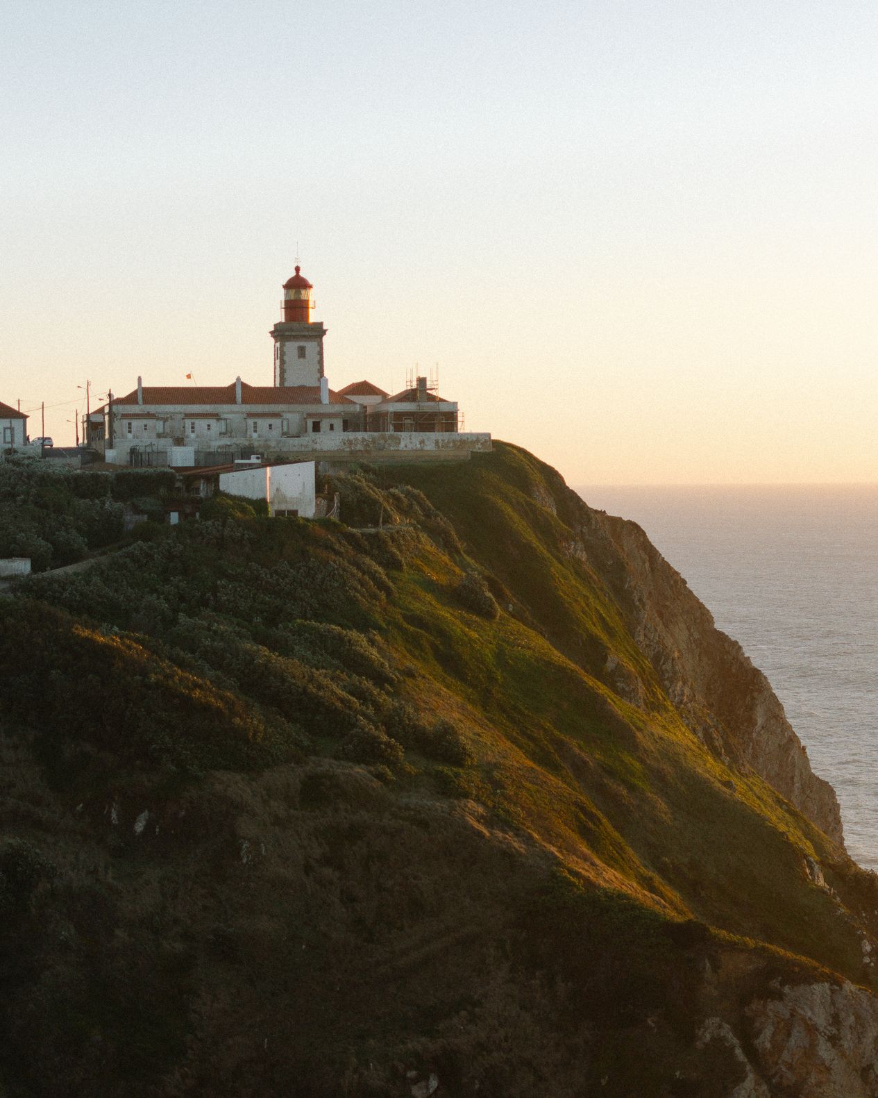 Cabo da Roca lighthouse perched on dramatic coastal cliffs at sunset with golden ocean horizon views.