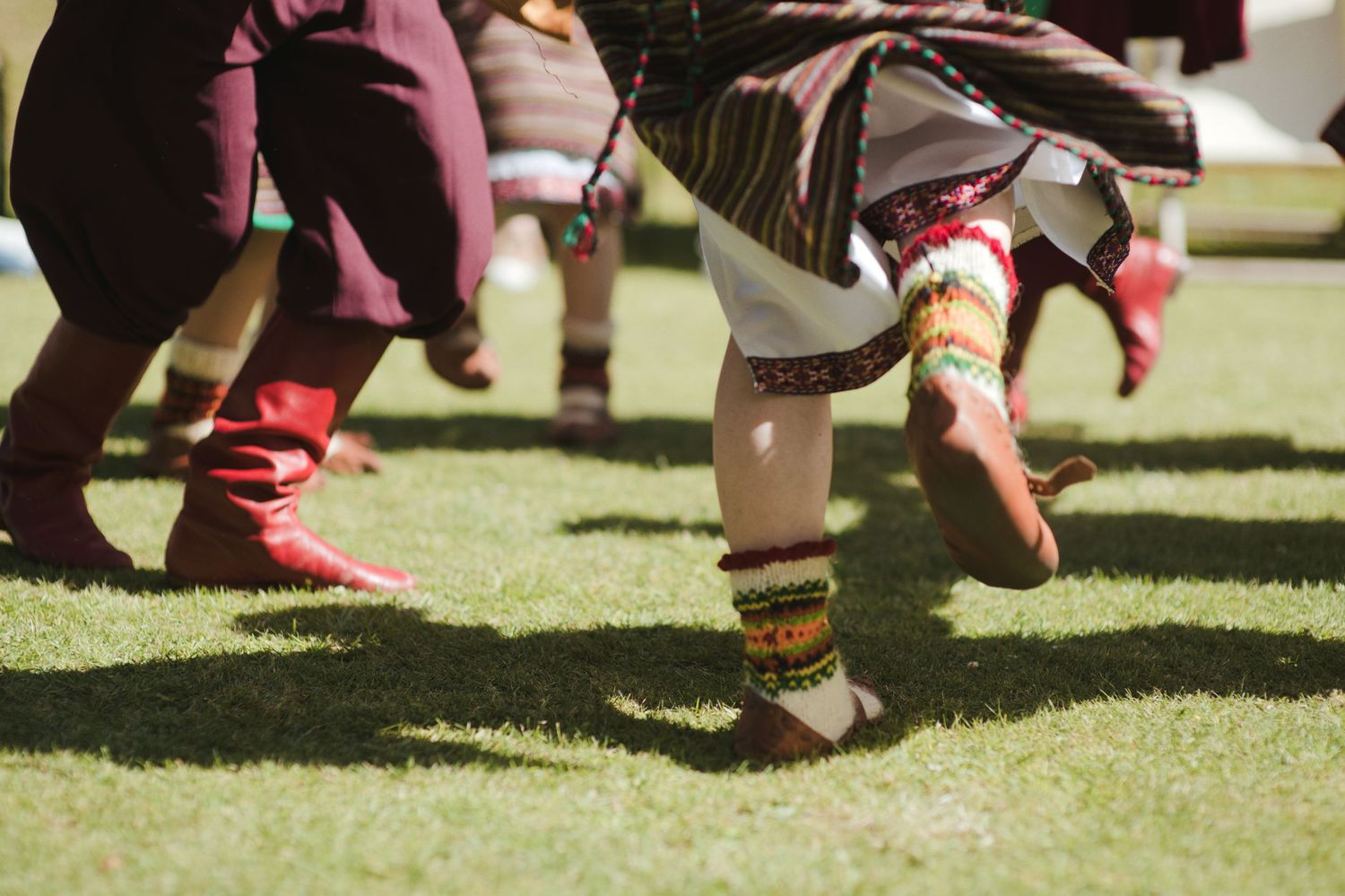 Traditional folk dancers performing on grass, wearing colorful ethnic costumes with decorative leg warmers and boots.