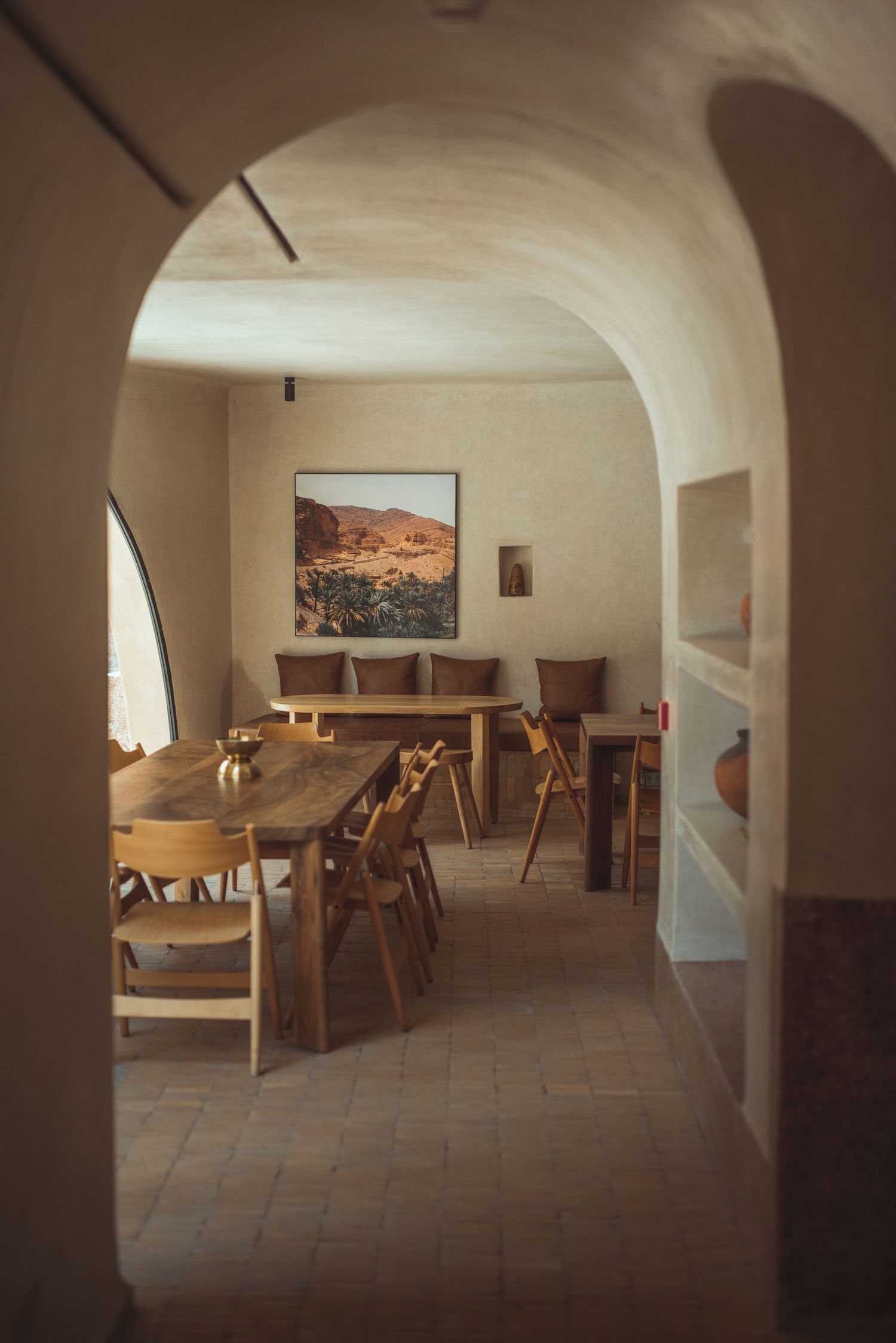 Warm earthy dining room viewed through an arched doorway with wooden furniture and desert artwork.