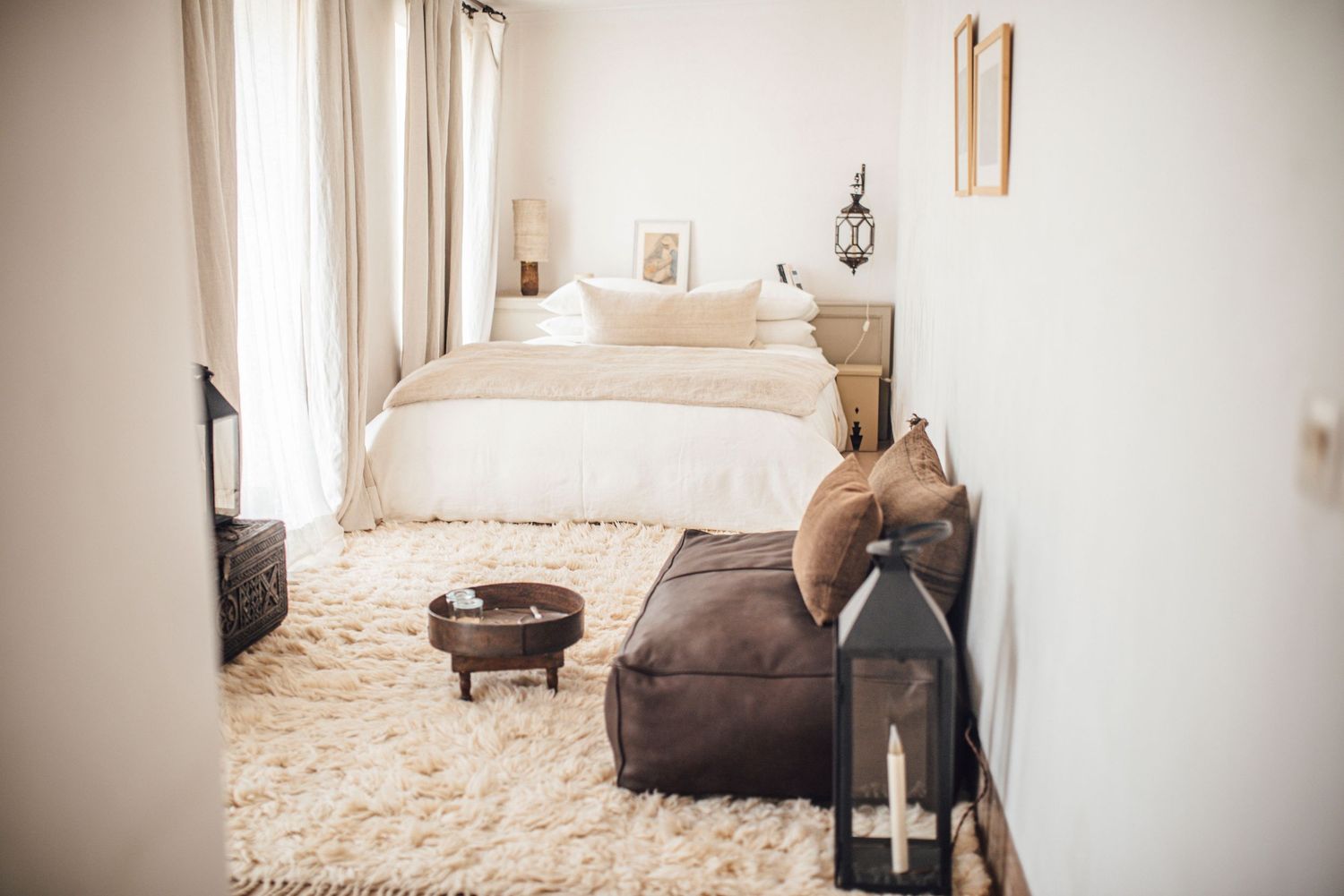 Cozy Moroccan-inspired bedroom with white walls, fluffy rug, brown bean bag, lantern, and neutral bedding.
