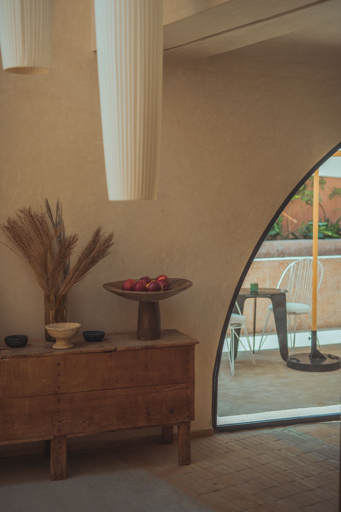 Rustic wooden dresser with dried pampas grass and red fruit bowl near an arched doorway.