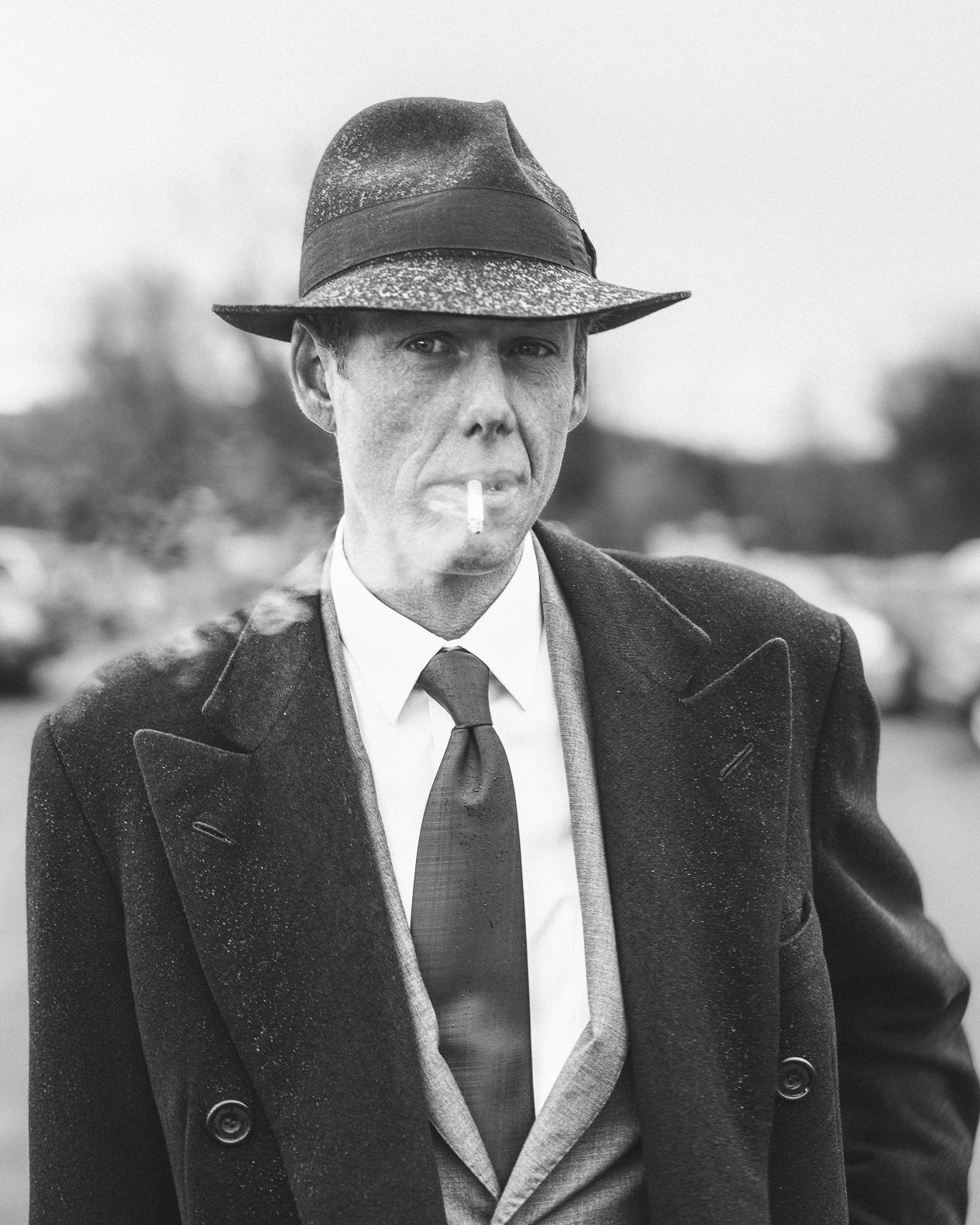 Vintage style black and white portrait of person in suit and fedora smoking a cigarette.