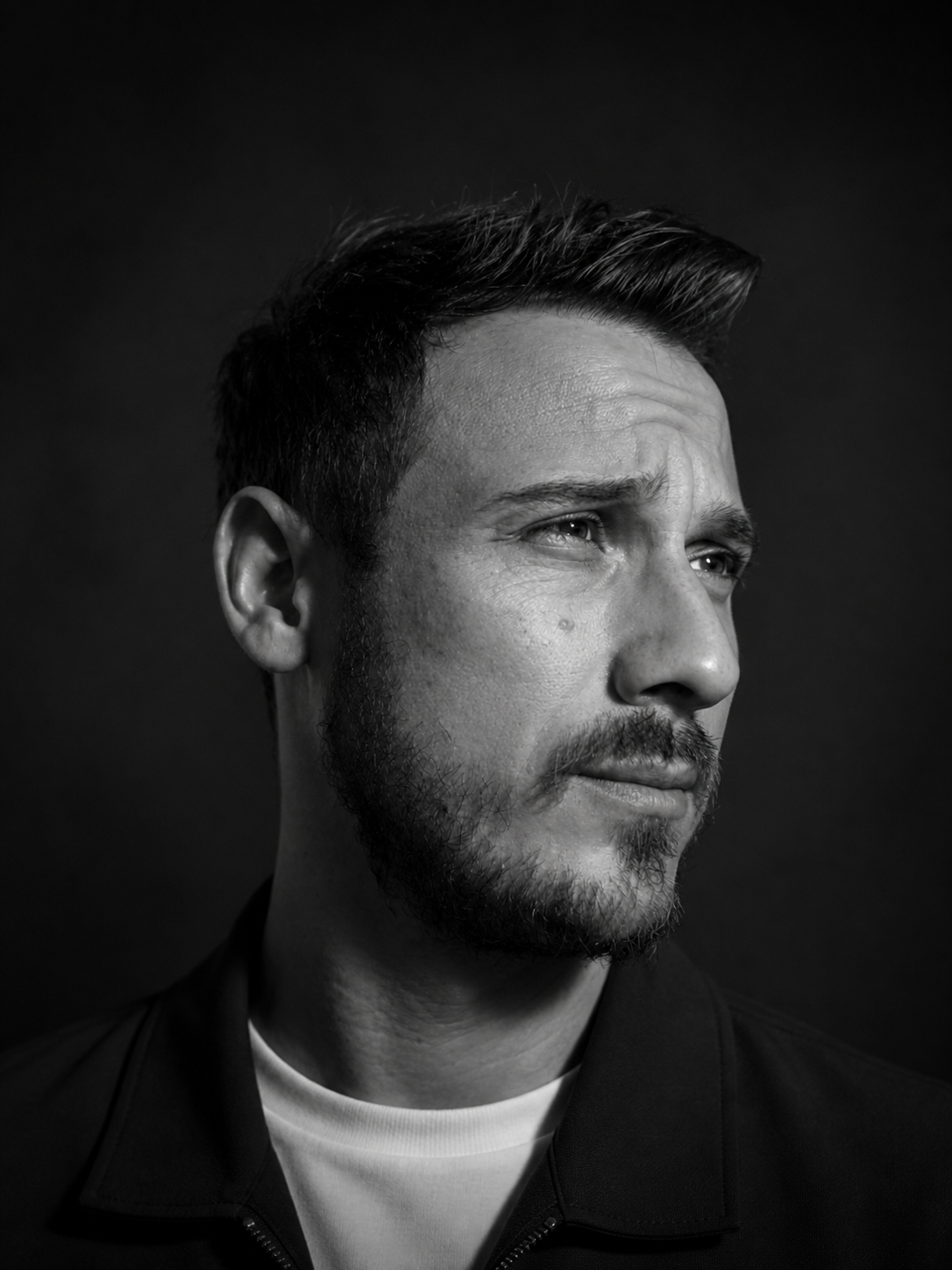Black and white dramatic portrait of thoughtful man with beard on dark background.