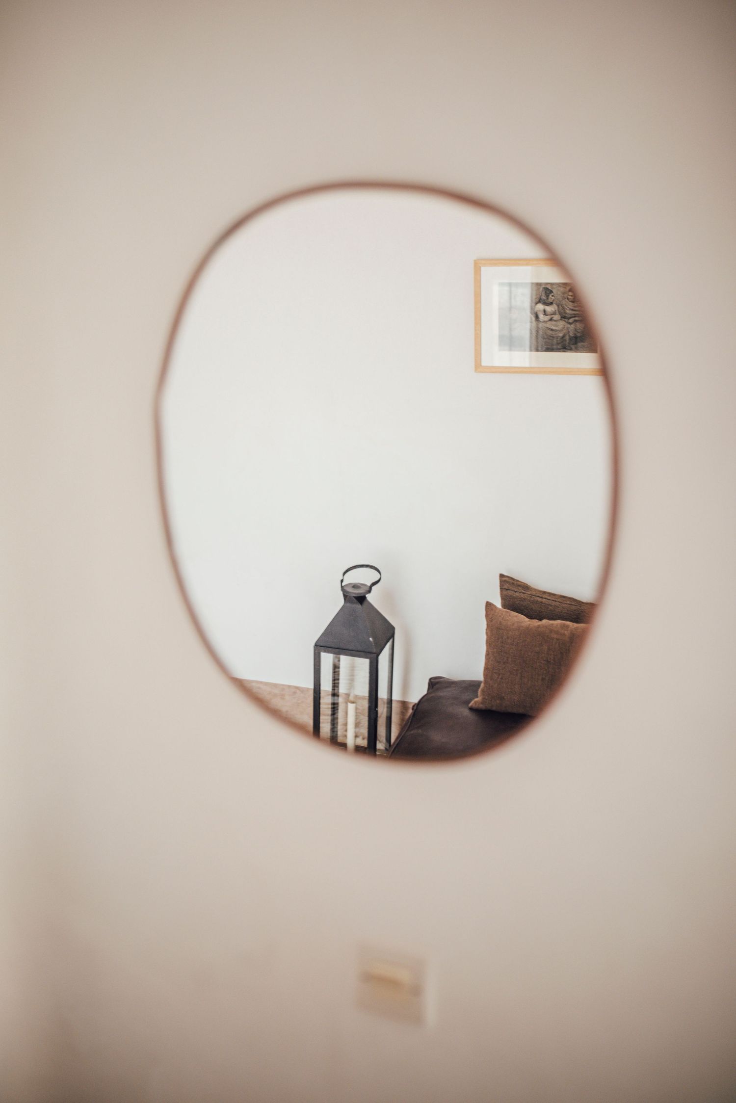 Oval mirror reflection showing lantern and cushions in neutral-toned room.