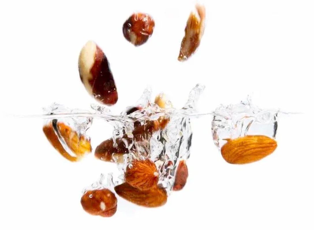 Assorted nuts including almonds and hazelnuts splashing into clear water against a white background.