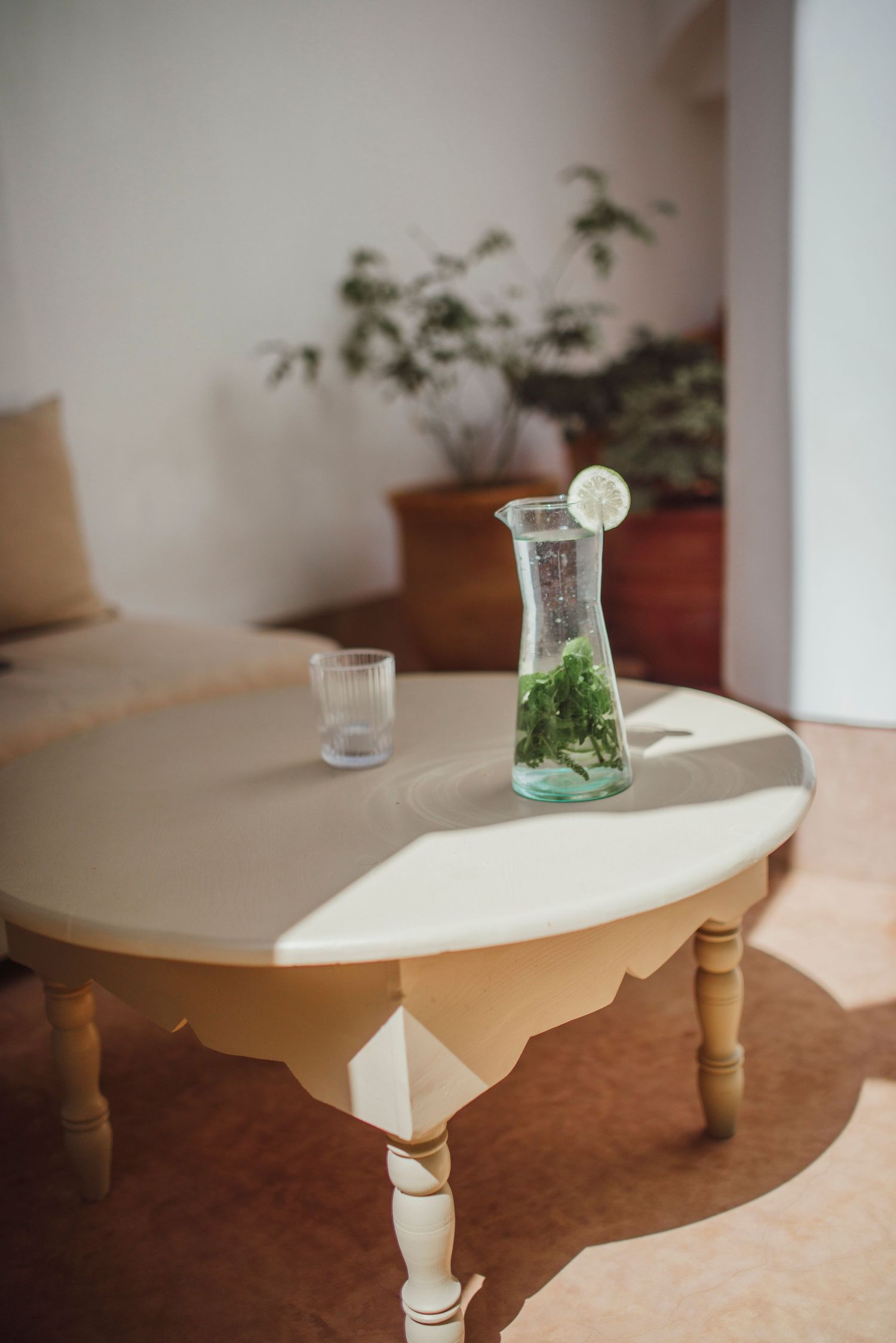 Glass carafe with mint and lemon on a vintage white coffee table in a sunlit room.