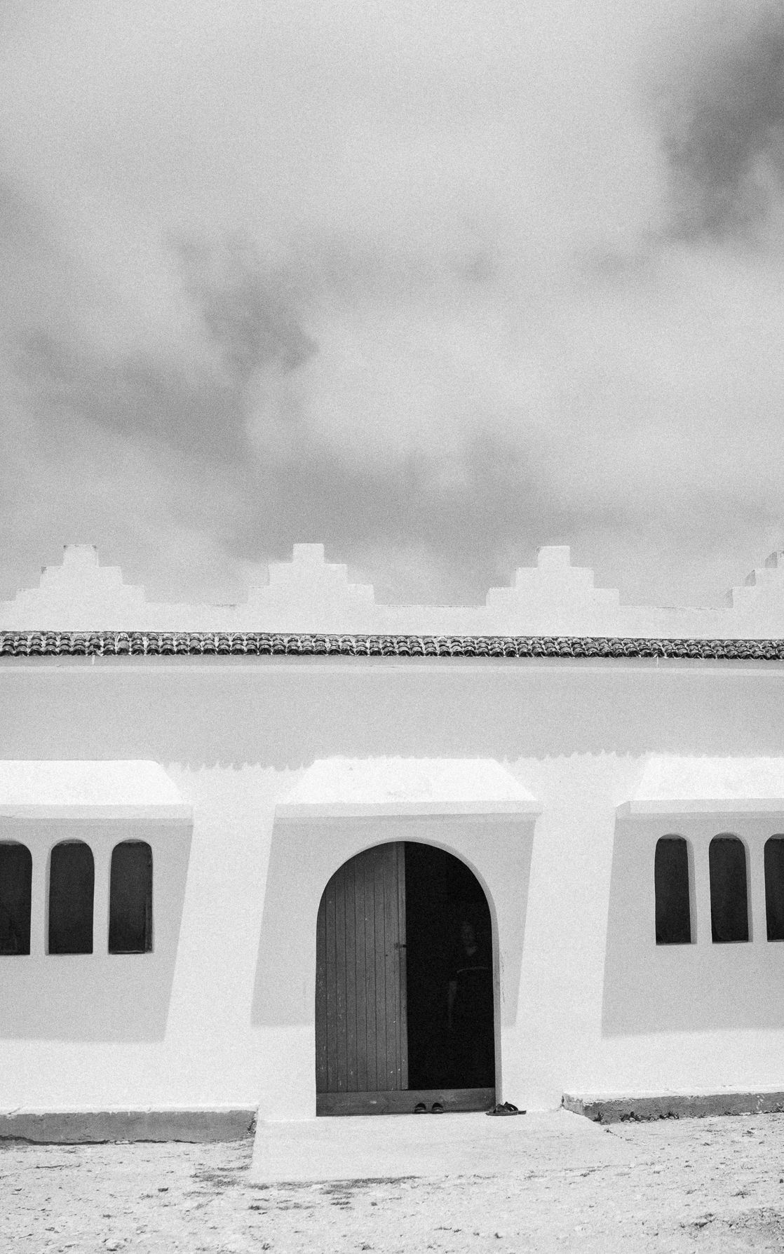 Black and white photo of a white Moorish-style building with arched windows and doorway under cloudy sky.