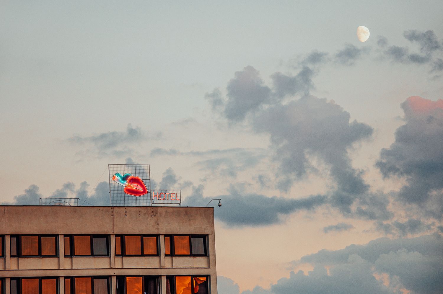 Colorful rooftop sign on a building at dusk with moon visible through soft pastel clouds.