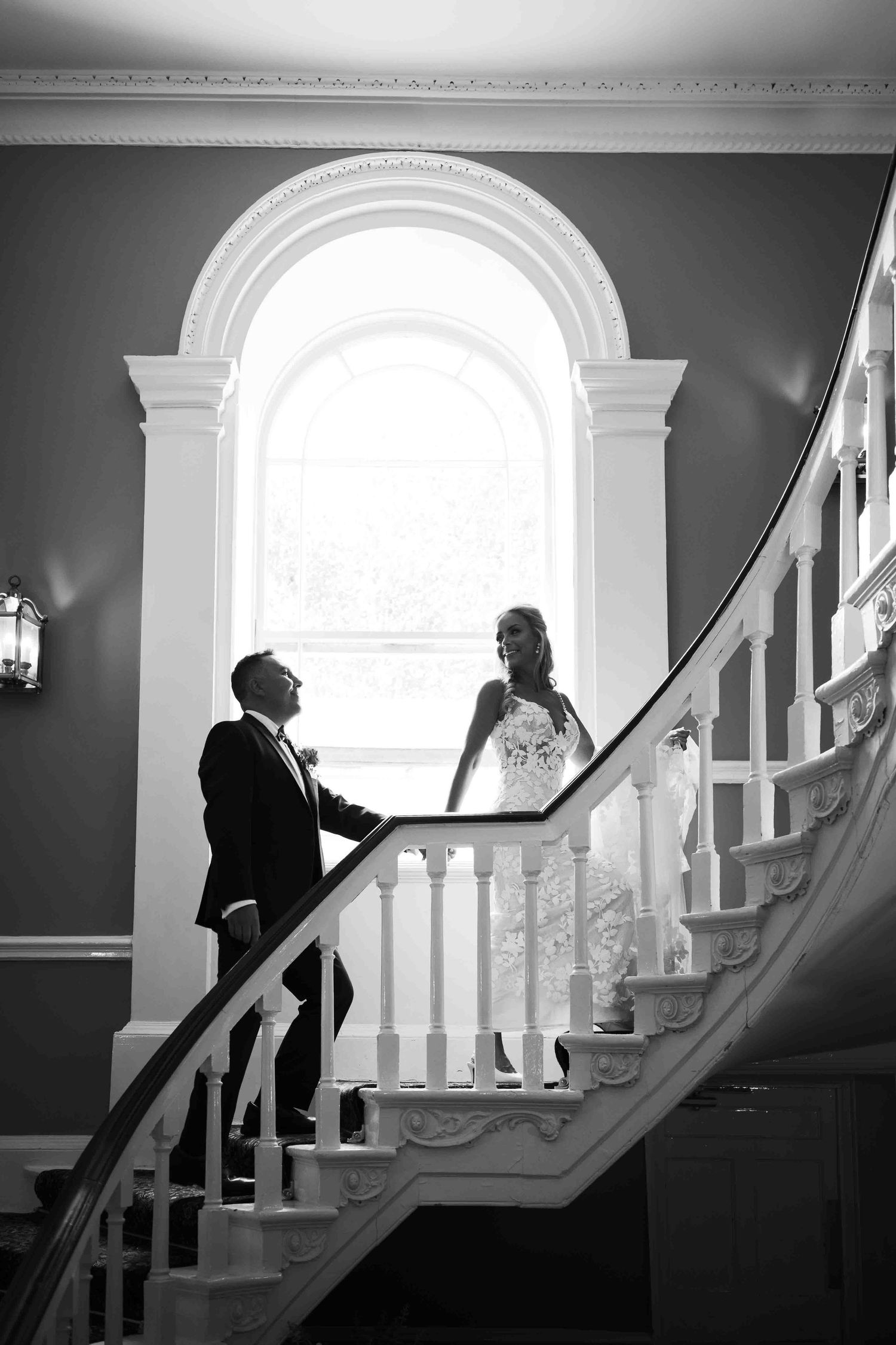 Elegant black and white photo of bride and groom on grand staircase by arched window. Dunboyne Castle