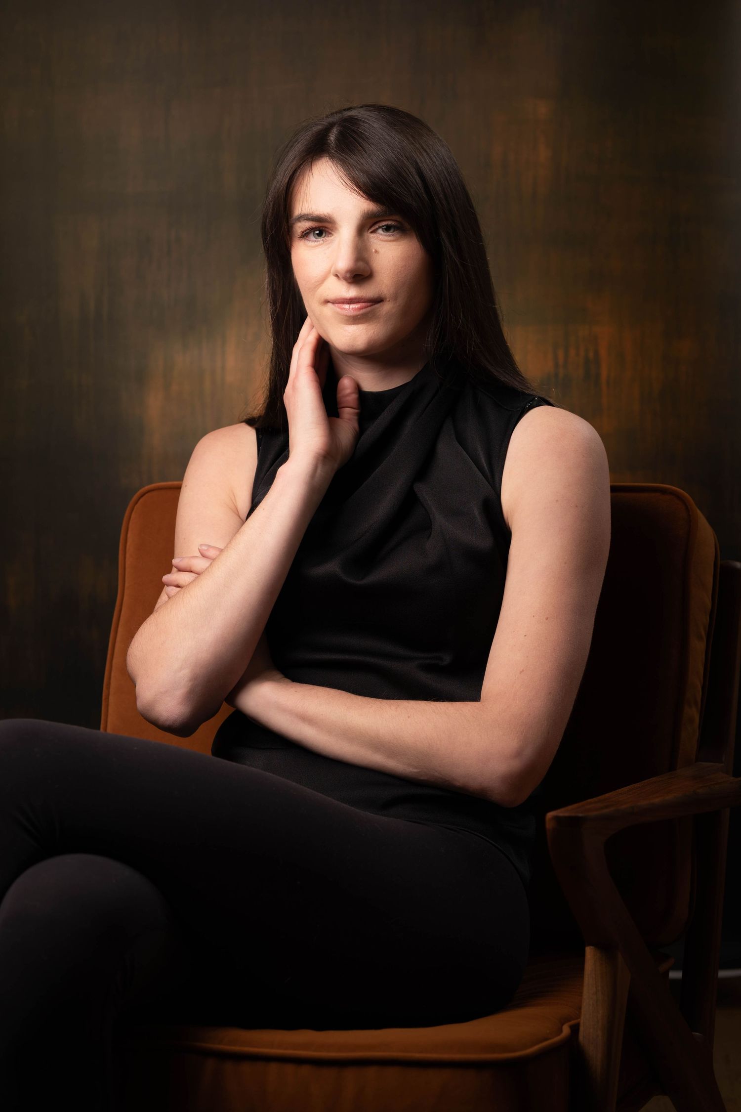 Elegant woman in black sleeveless top seated in wooden chair posing for studio portrait photography. Portrait Photography Ireland