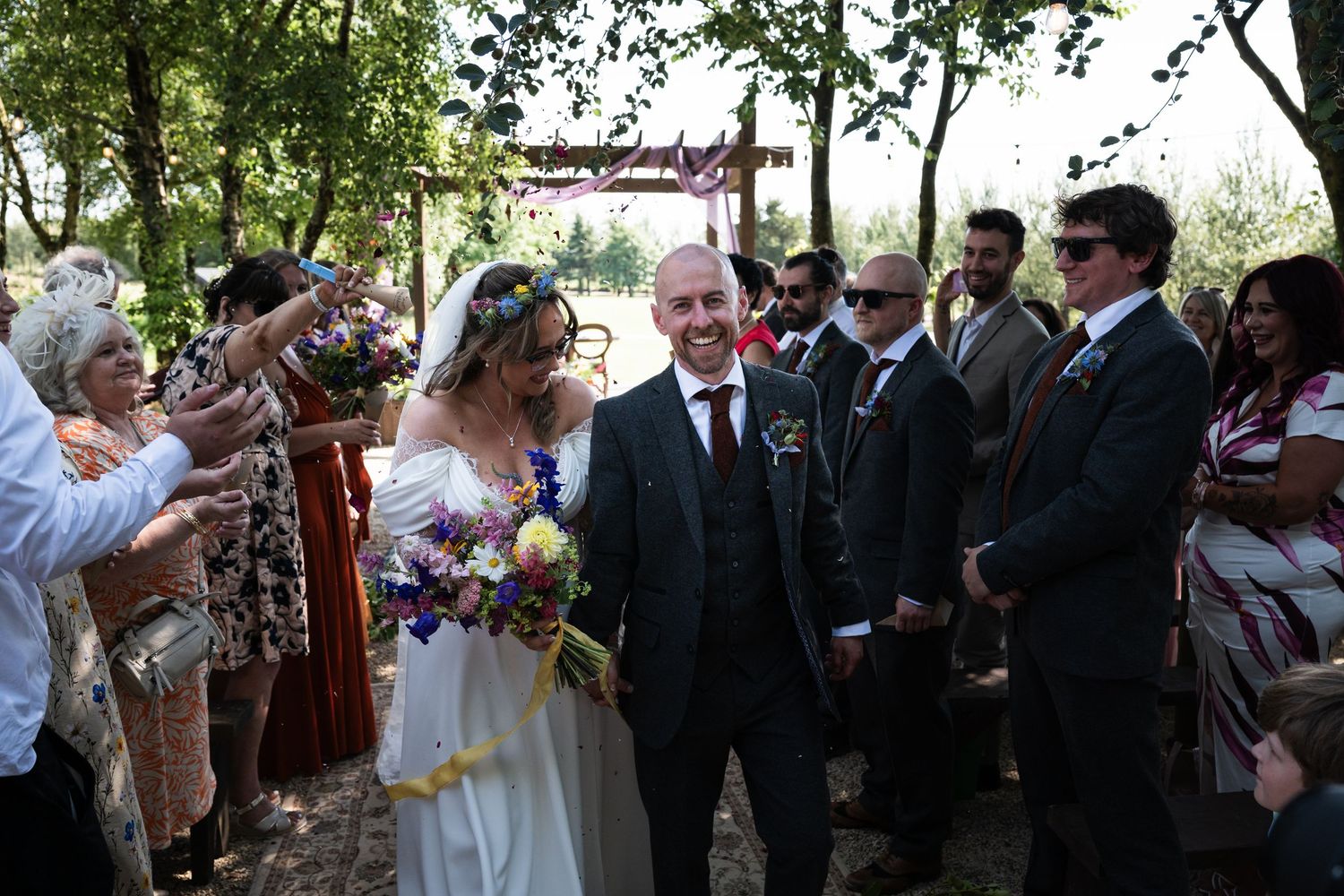 Bride and groom walk through cheering guests after outdoor wedding ceremony with colourful bouquet. Mountain View, Kilkenny