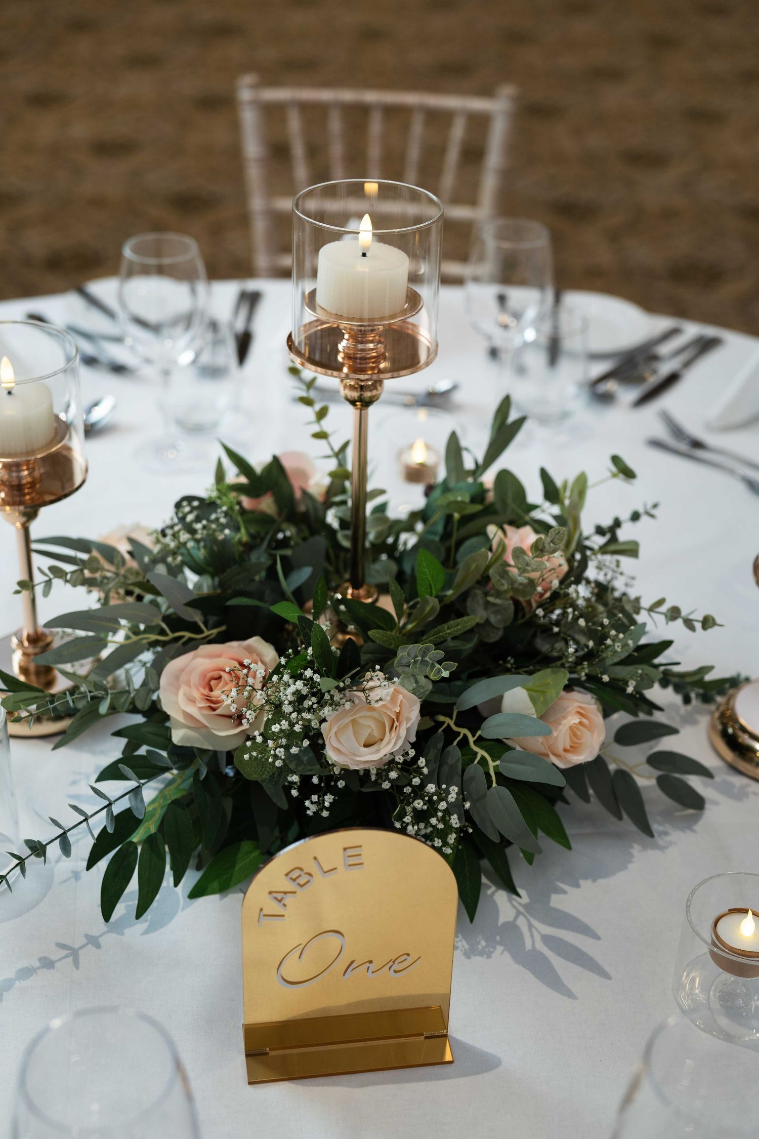 Elegant wedding table centerpiece with blush roses, greenery, gold candleholders, and a gold Table One sign on white linen. Dunboyne Castle