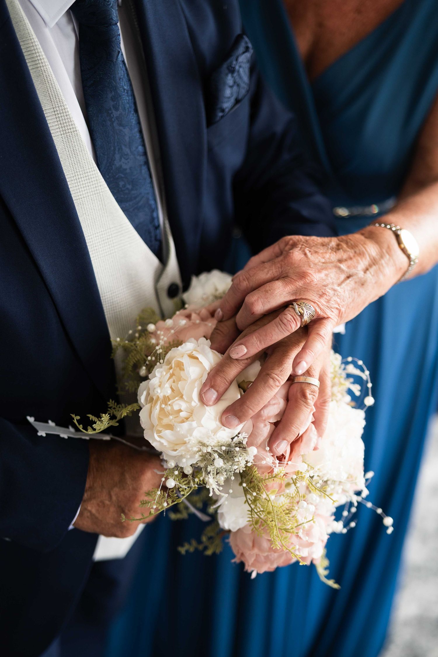 Elderly couple holds hands over a white peony wedding bouquet showing wedding rings. Irish wedding photography. Dunboyne Castle