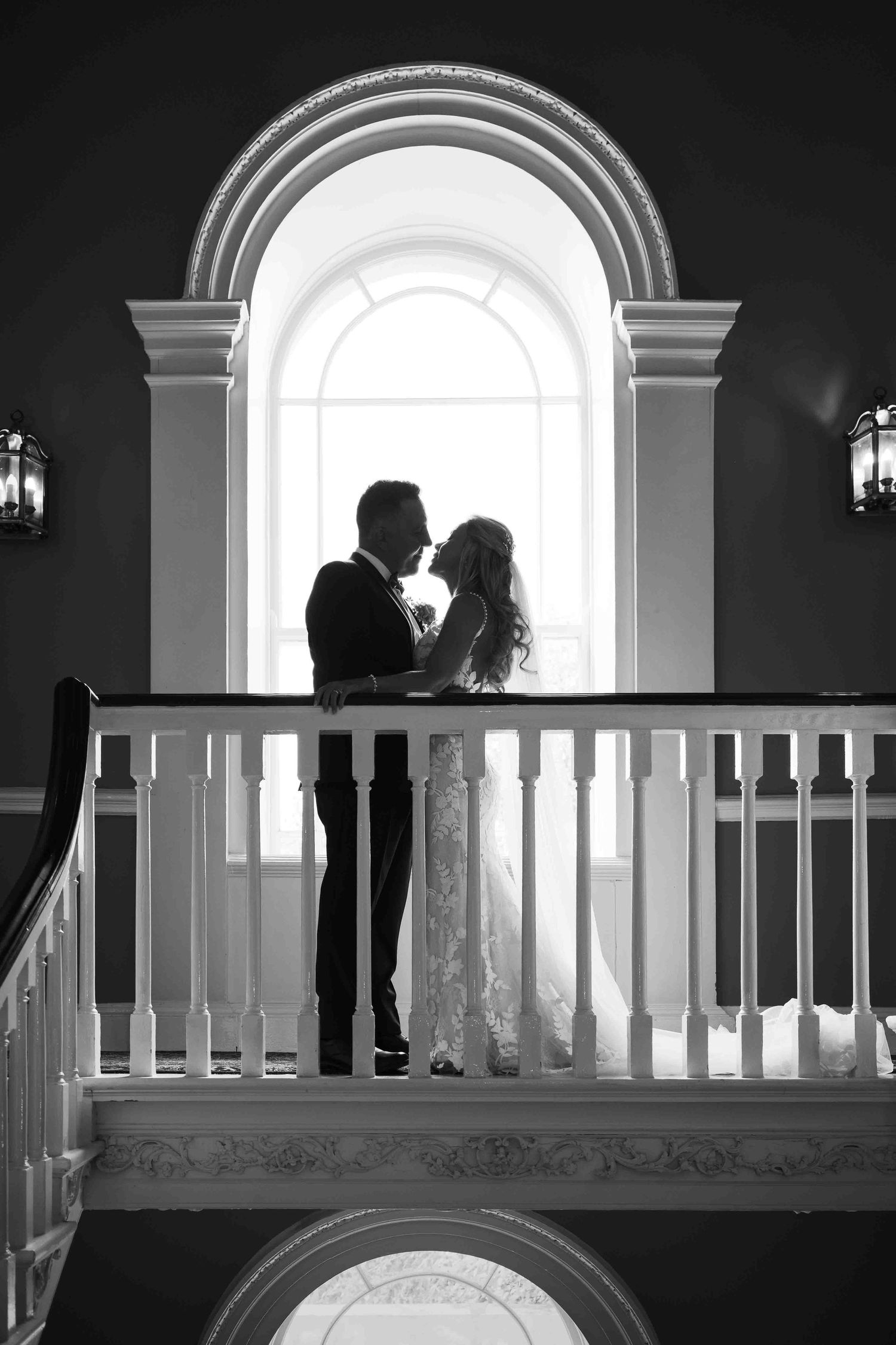 Black and white silhouette of bride and groom embracing before a grand arched window. Dunboyne Castle