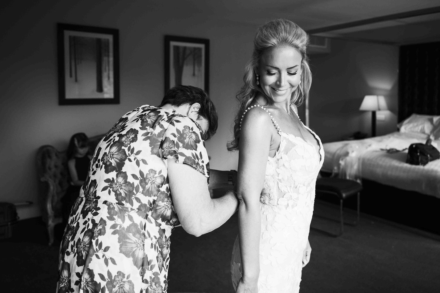 Mother helps smiling bride fasten wedding dress in black and white bridal preparation photo. Dunboyne Castle