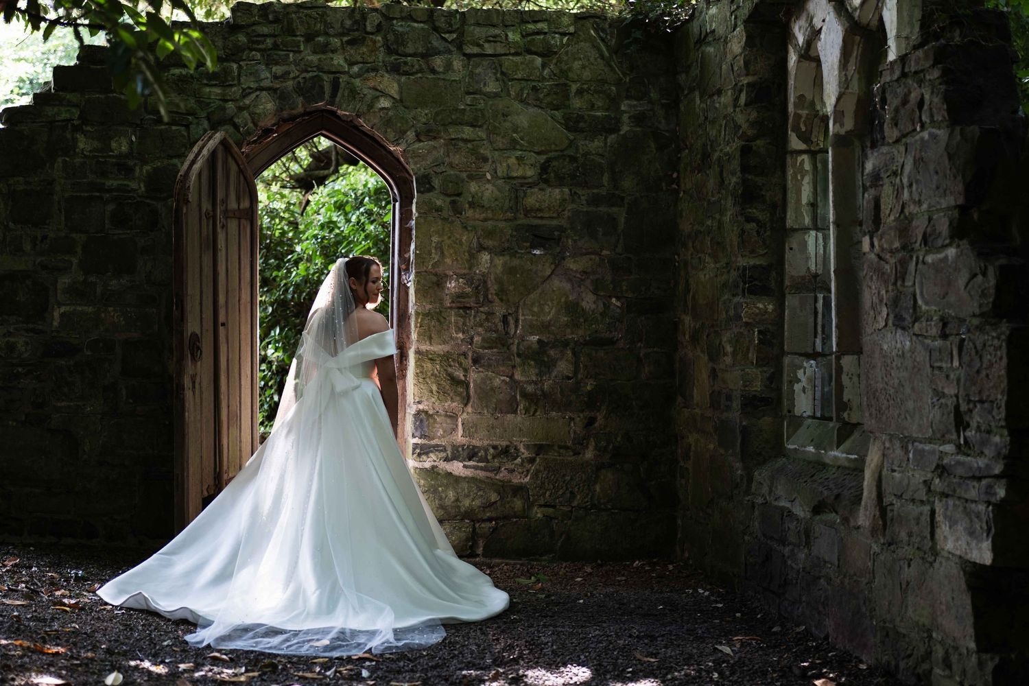 Bride in white gown and veil standing in stone archway doorway of rustic castle ruins on wedding day. Dunboyne Castle