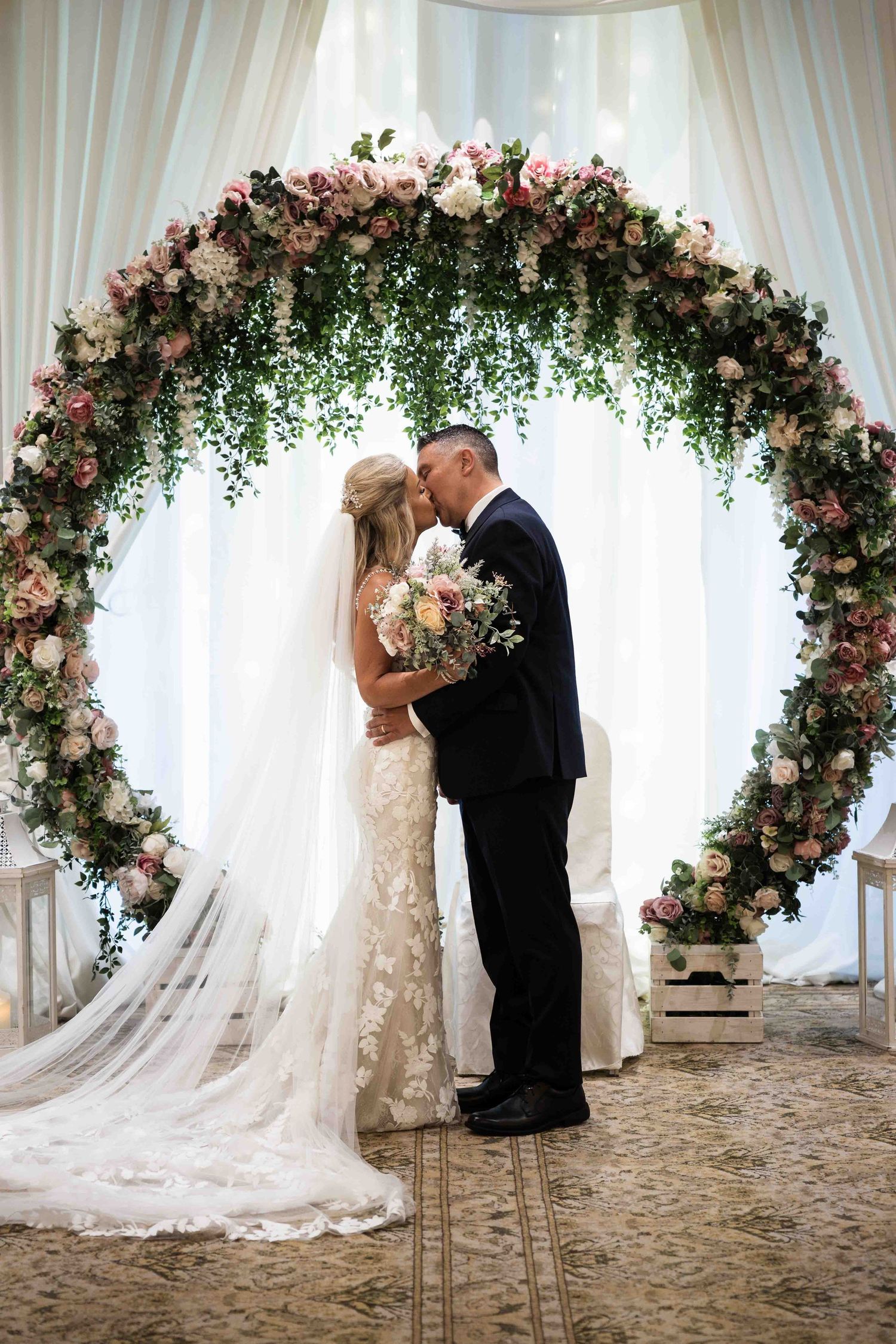 Bride and groom share first kiss under a stunning circular floral arch adorned with pink roses. Dunboyne Castle