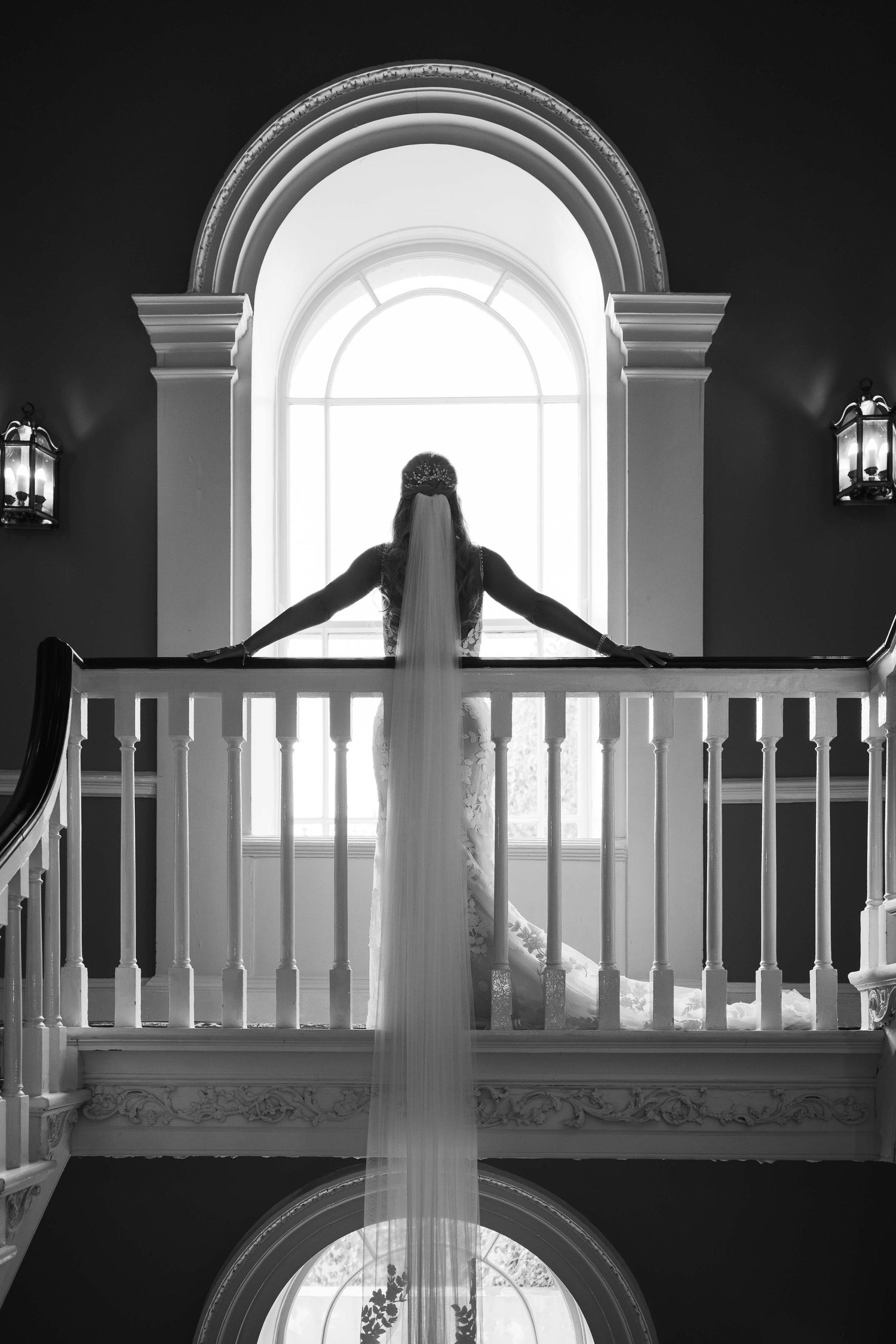 Bride standing on a grand staircase balcony, veil cascading down in black and white. Irish wedding photography. Dunboyne Castle