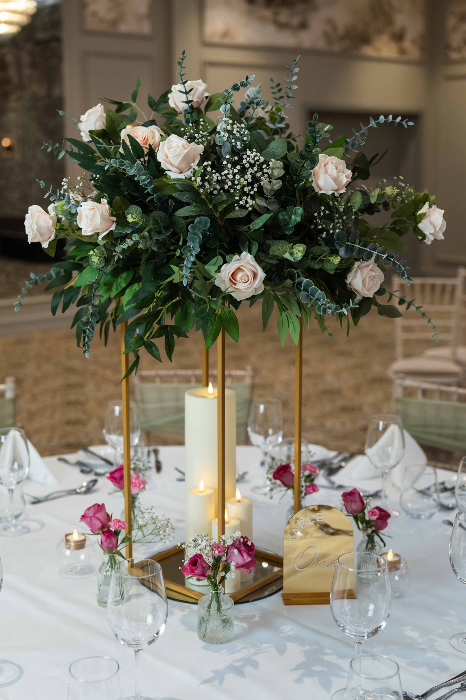 Elegant wedding table centerpiece with white roses, greenery on gold stand, candles, and pink roses in glass vases. Dunboyne Castle