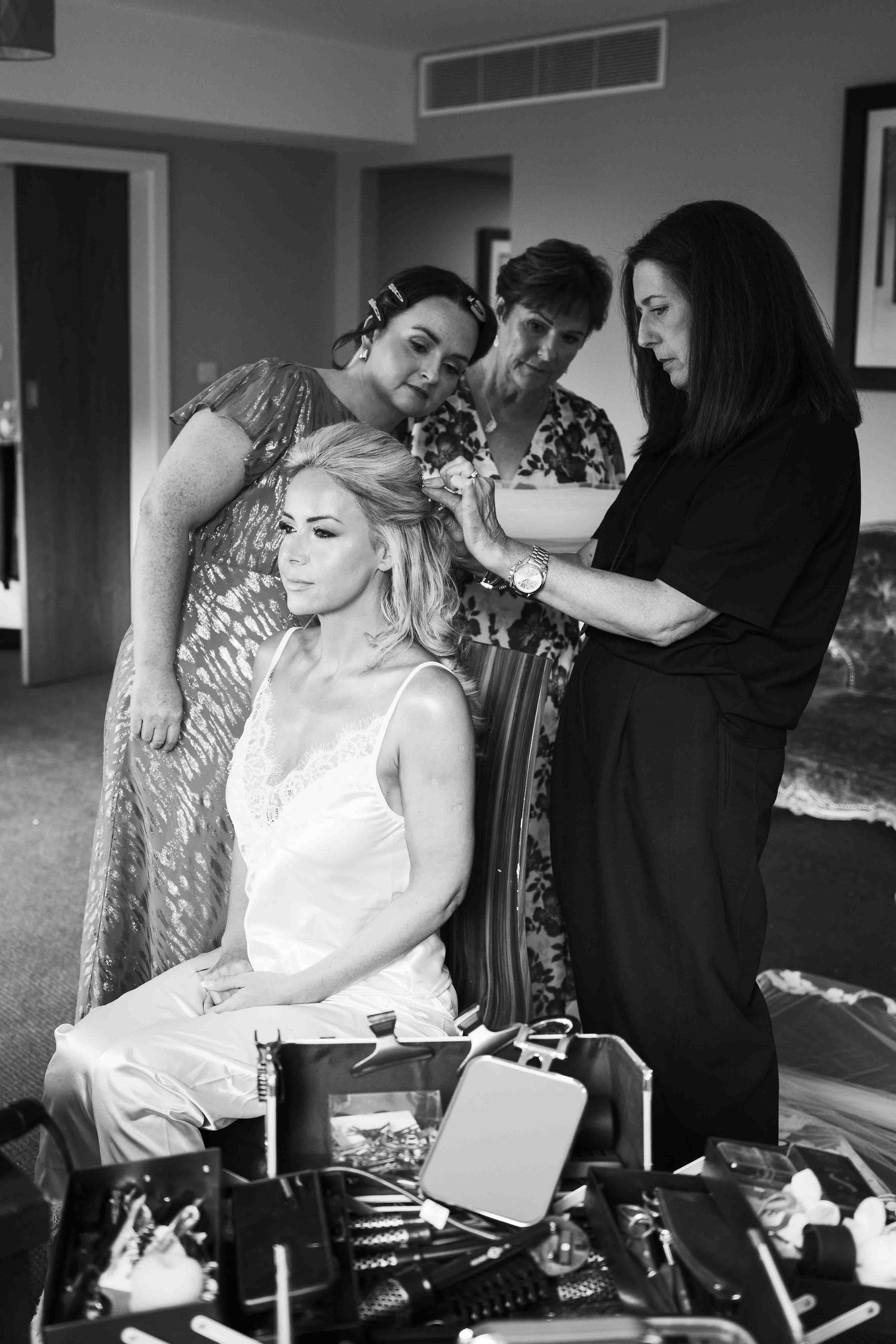 Bride gets hair styled by professionals while family watches in black and white wedding preparation photo. Dunboyne Castle