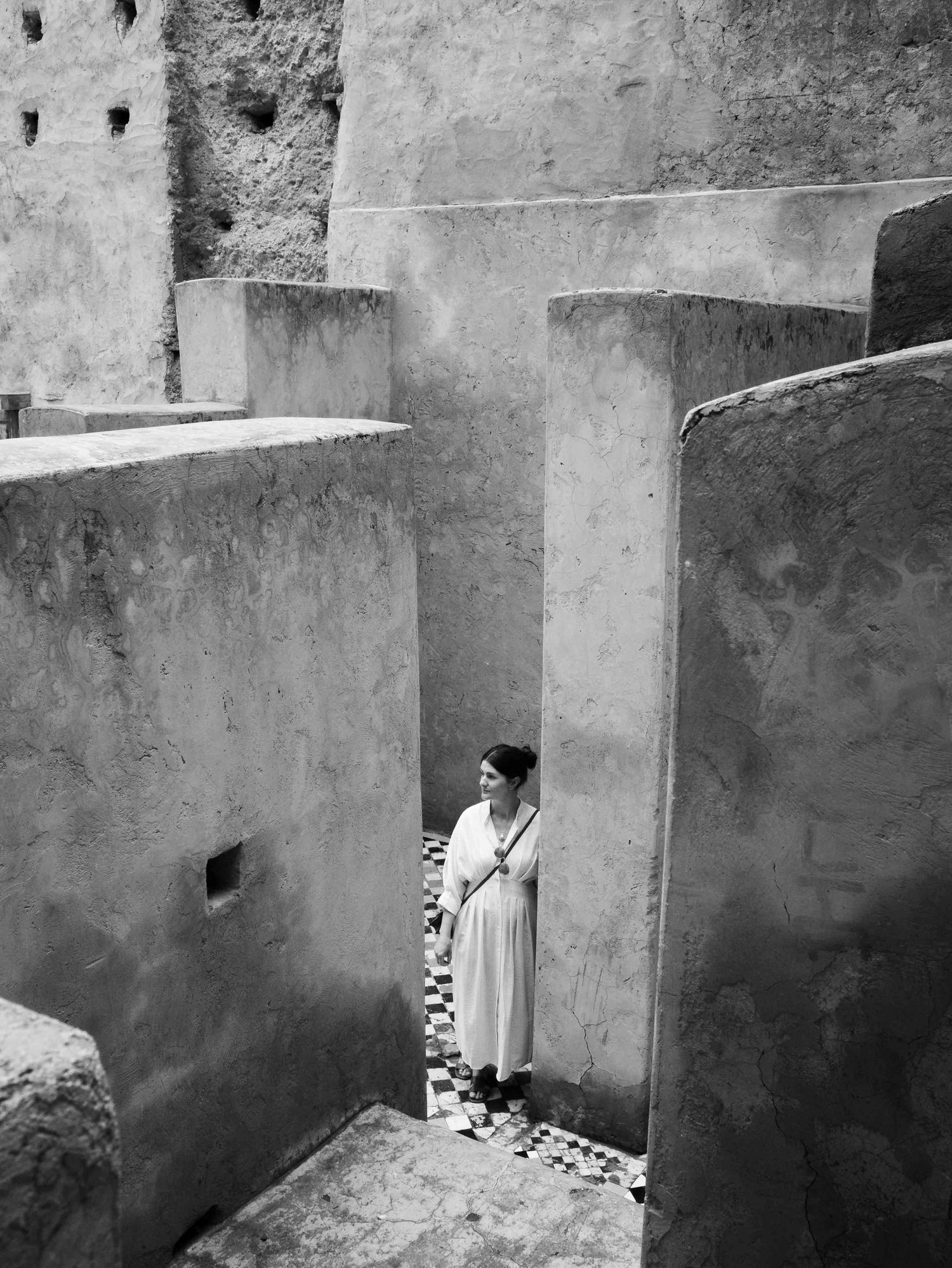 Black and white aerial view of a woman in white dress standing in ancient earthen maze-like ruins.