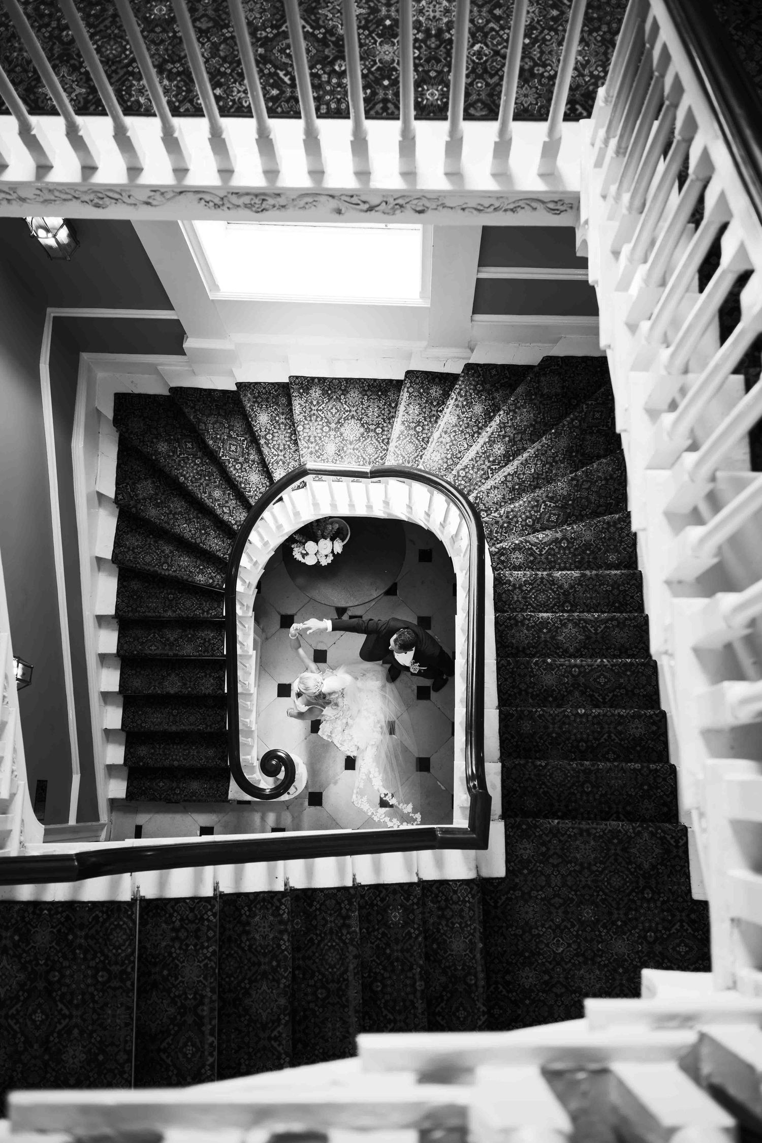 Aerial black and white view of a bride and groom at the base of an elegant spiral staircase. Dunboyne Castle