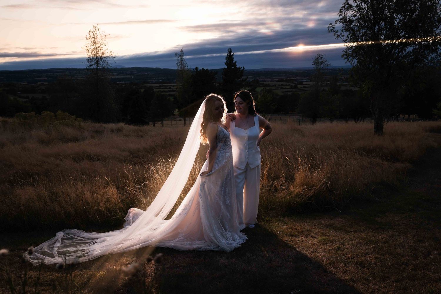 Two brides in white gowns stand together at sunset in a scenic outdoor landscape. Irish wedding photography. Mountain View, Kilkenny