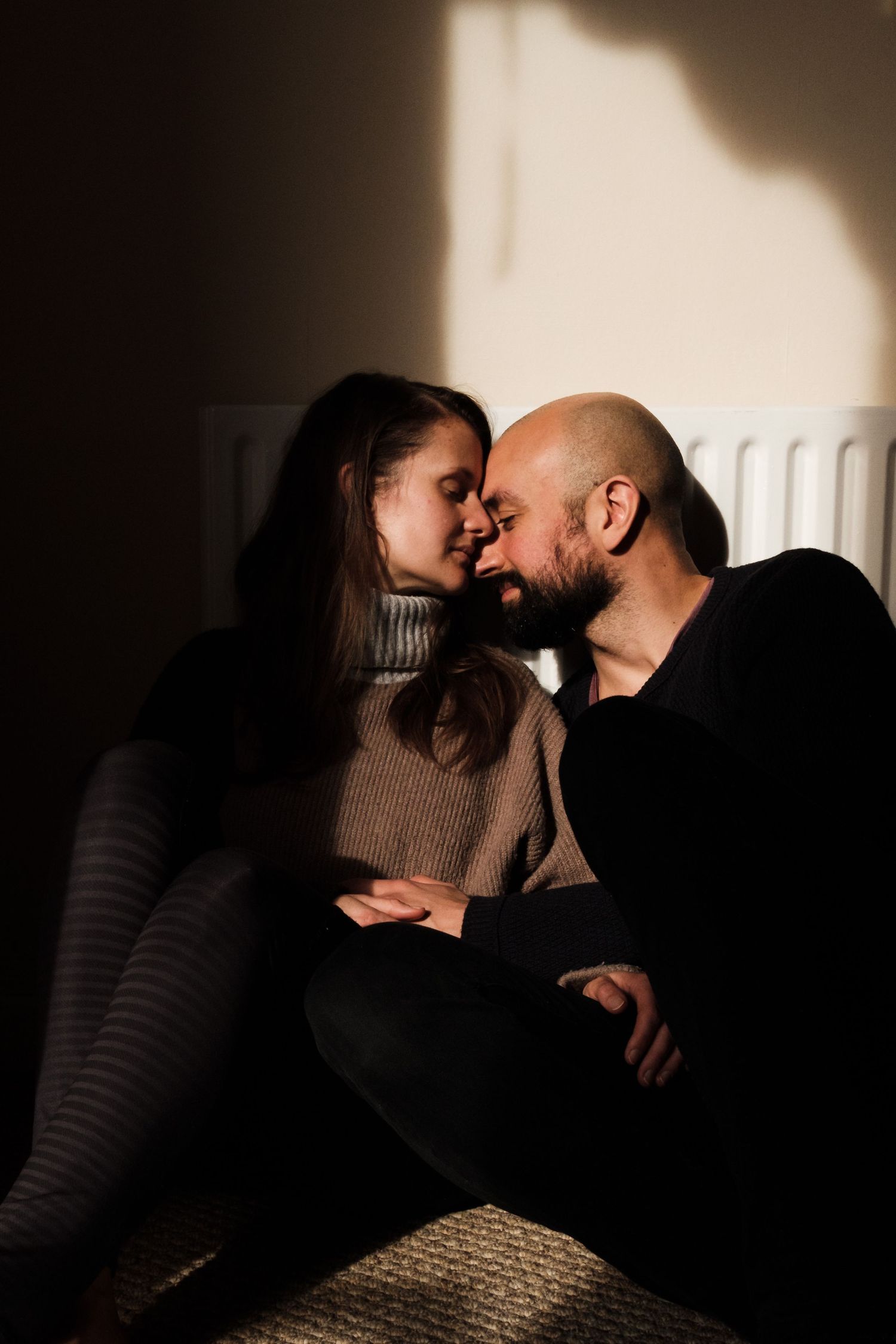 Couple sharing a tender moment, foreheads touching, bathed in dramatic natural light in a dark room. Portrait Photography Ireland