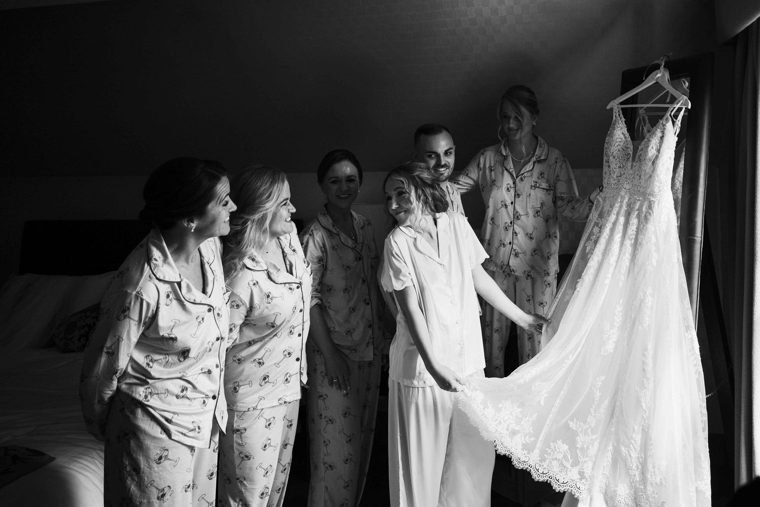 Bridesmaids in floral pajamas admire a stunning wedding dress in a black and white photo. Irish wedding photography. Langtons, Kilkenny
