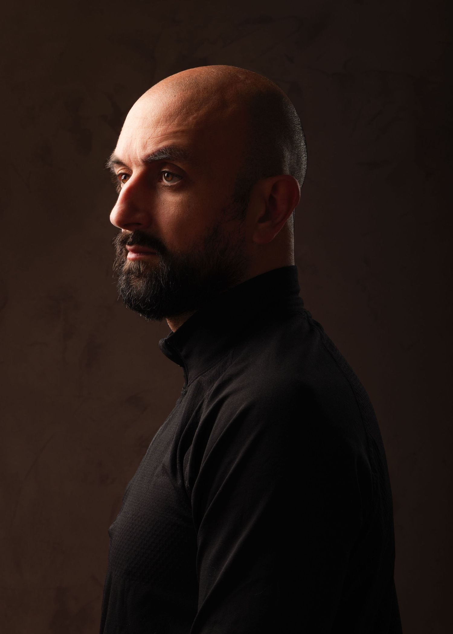 Side profile portrait of a bald bearded man in a black turtleneck against a dark background. Portrait Photography Ireland