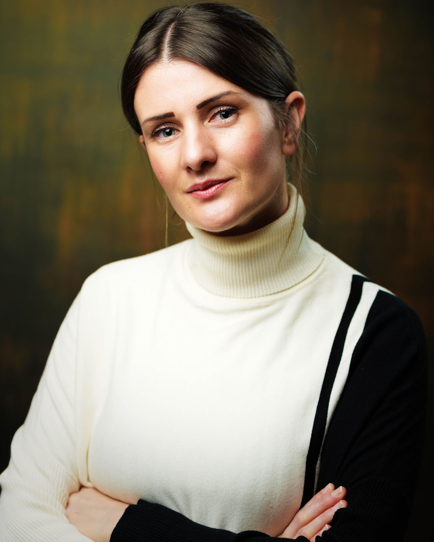 Young brunette woman in white turtleneck and black cardigan with arms crossed against dark background. Portrait Photography Ireland