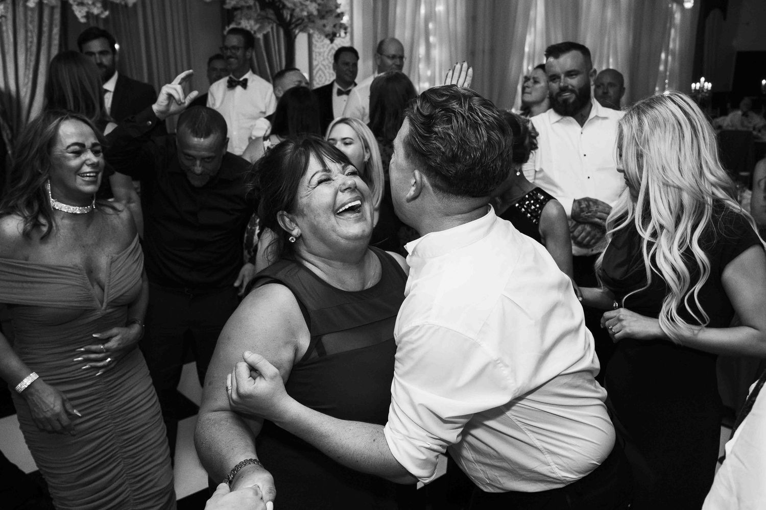 Black and white photo of joyful wedding guests dancing and laughing at a lively reception.  Queer wedding. Clontarf Castle